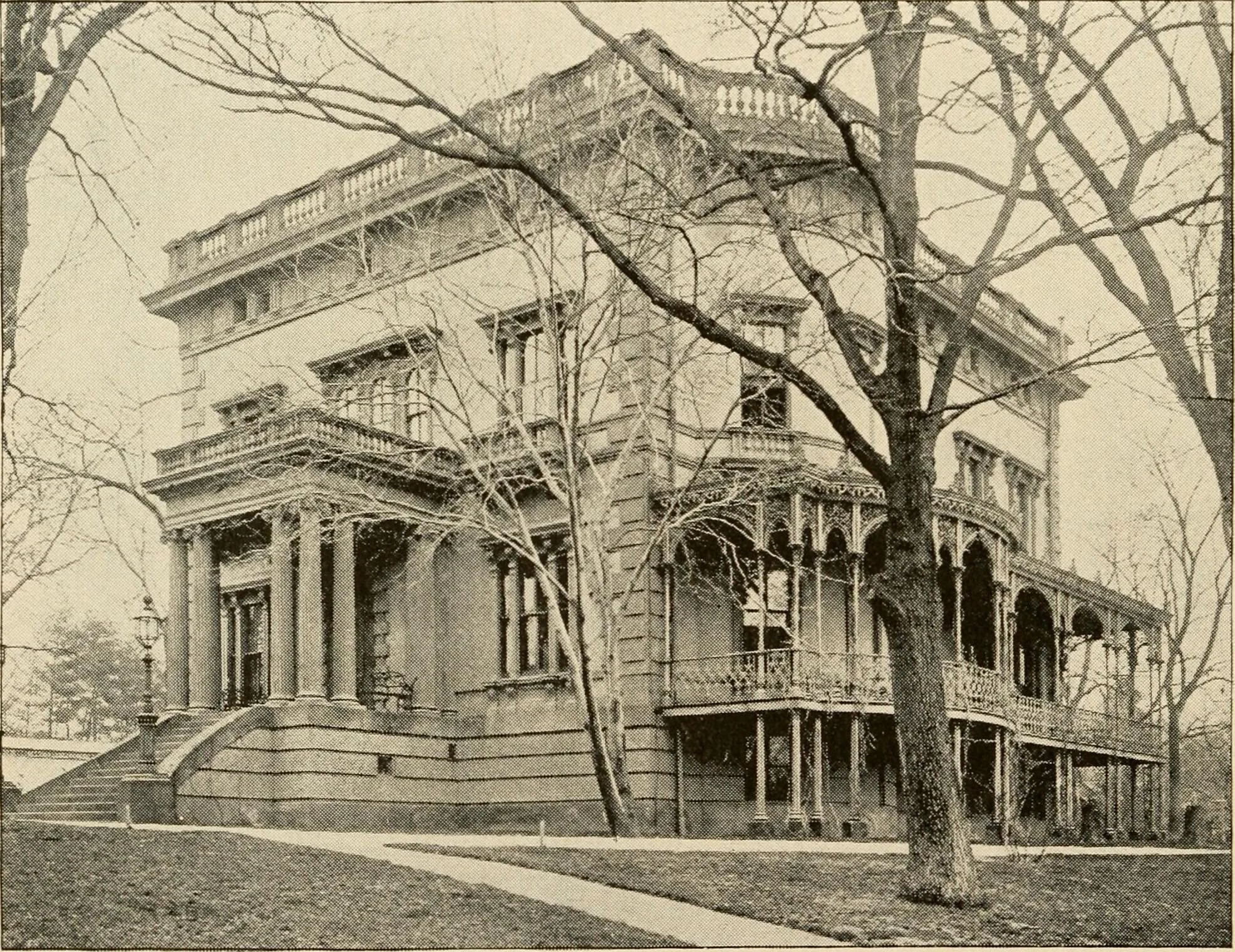 A large, old mansion with classical architectural features including columns, multiple balconies, and ornate decorations. The house is surrounded by leafless trees and is accessed by a set of stairs with a curved railing.