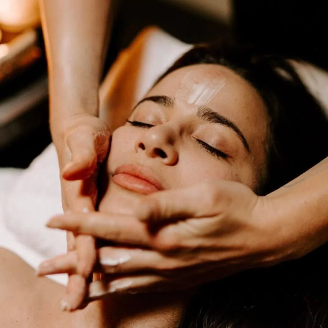 A woman with a peaceful expression receiving a facial massage in a spa setting.