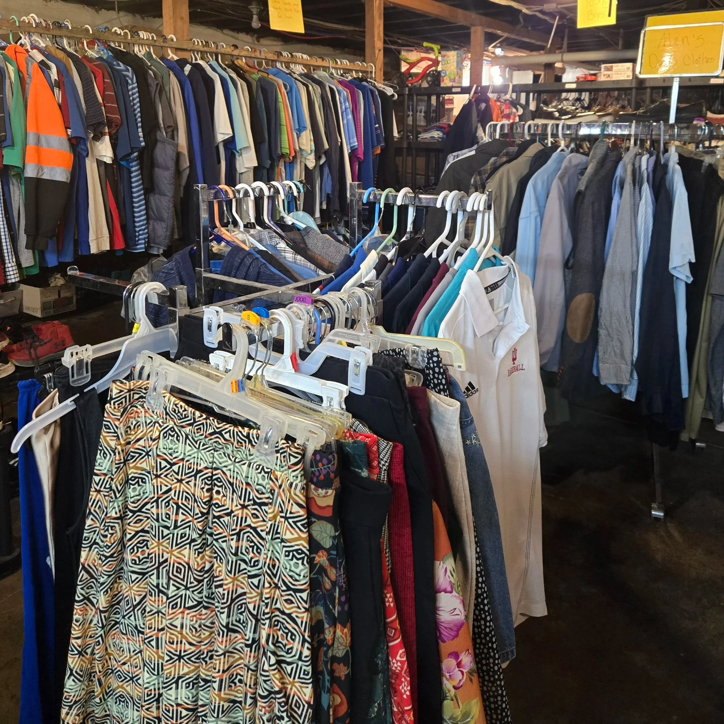 Clothing racks with men's and women's shirts, pants, and jackets inside a thrift store or clothing shop.