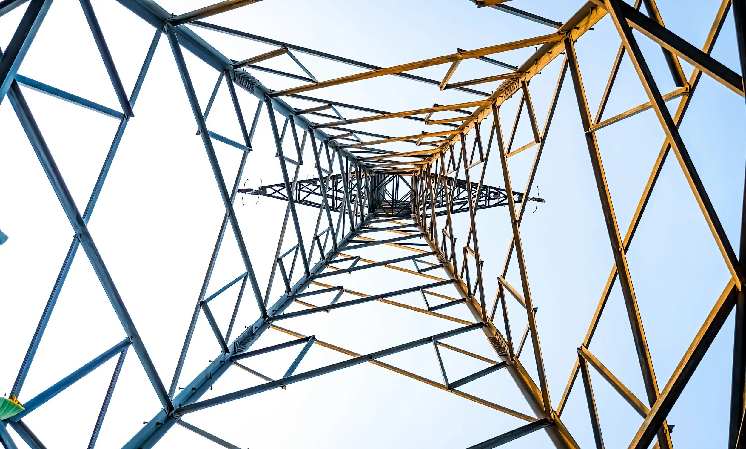 Looking up at a tall radio tower from below, showing a lattice of metal beams and antennas against a clear sky.