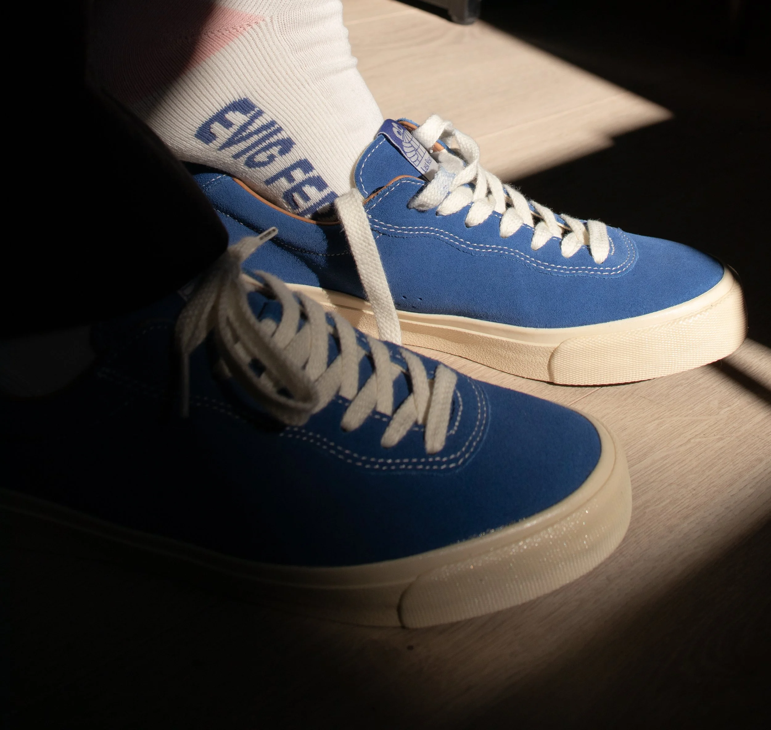 Nærbilde av en blå sneakers med hvite liss og en hvit sokk med blå tekst som sier EVIG FERIE