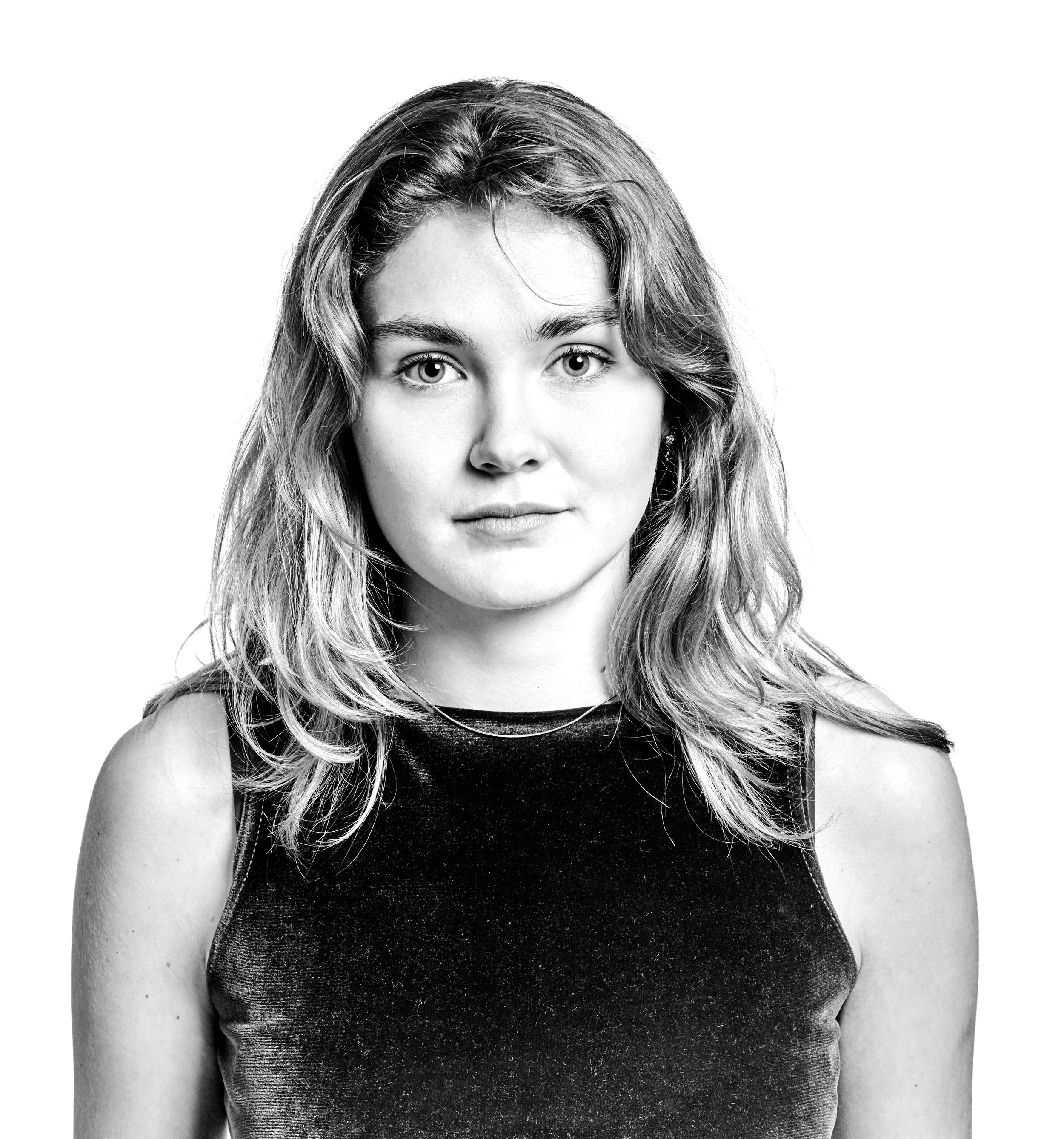 Black and white portrait of a young woman with shoulder-length wavy hair wearing a sleeveless dark top, looking directly at the camera with a neutral expression.