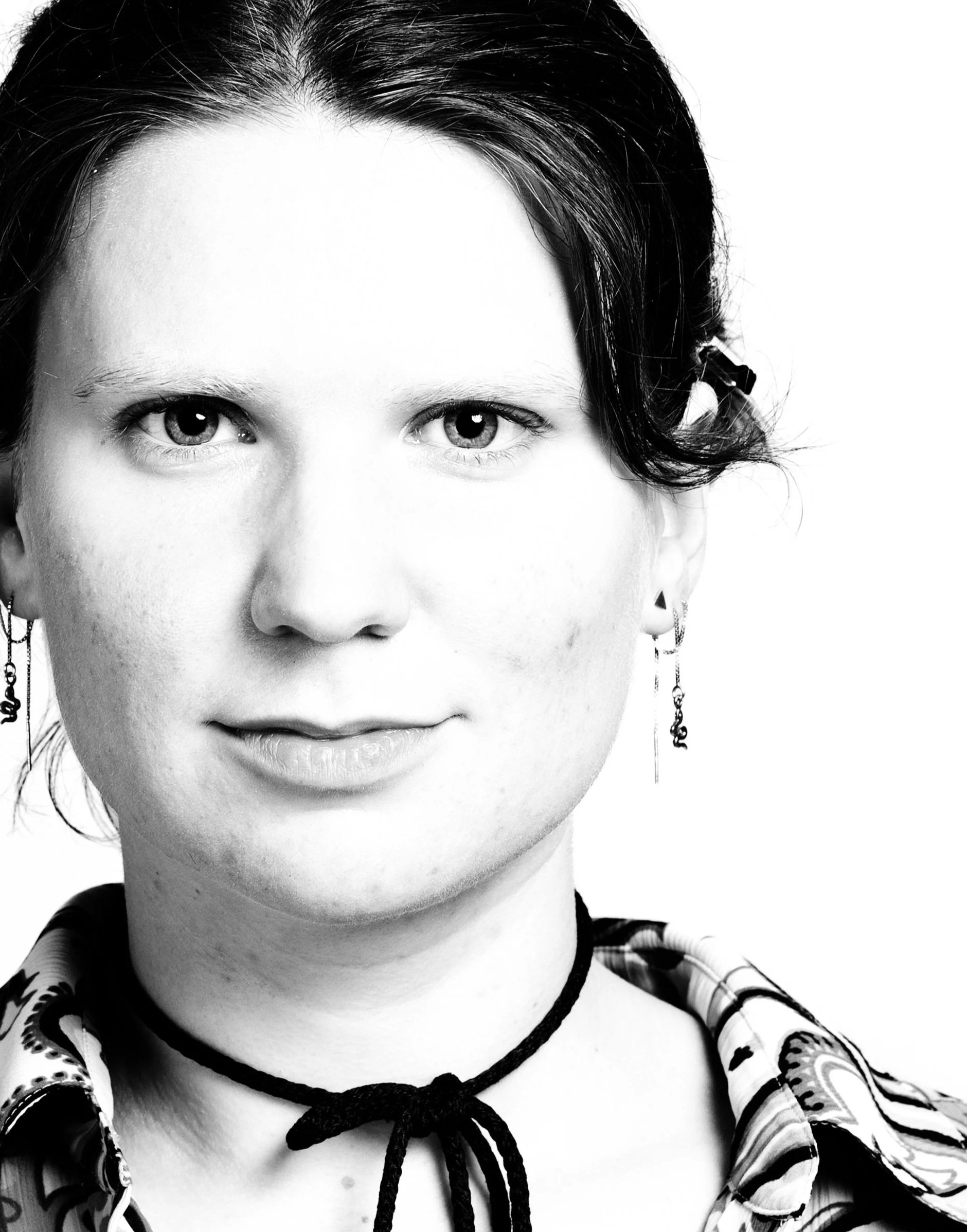 A black and white portrait of a woman with dark hair, light skin, earrings, wearing a patterned shirt, and a bow tie necklace.