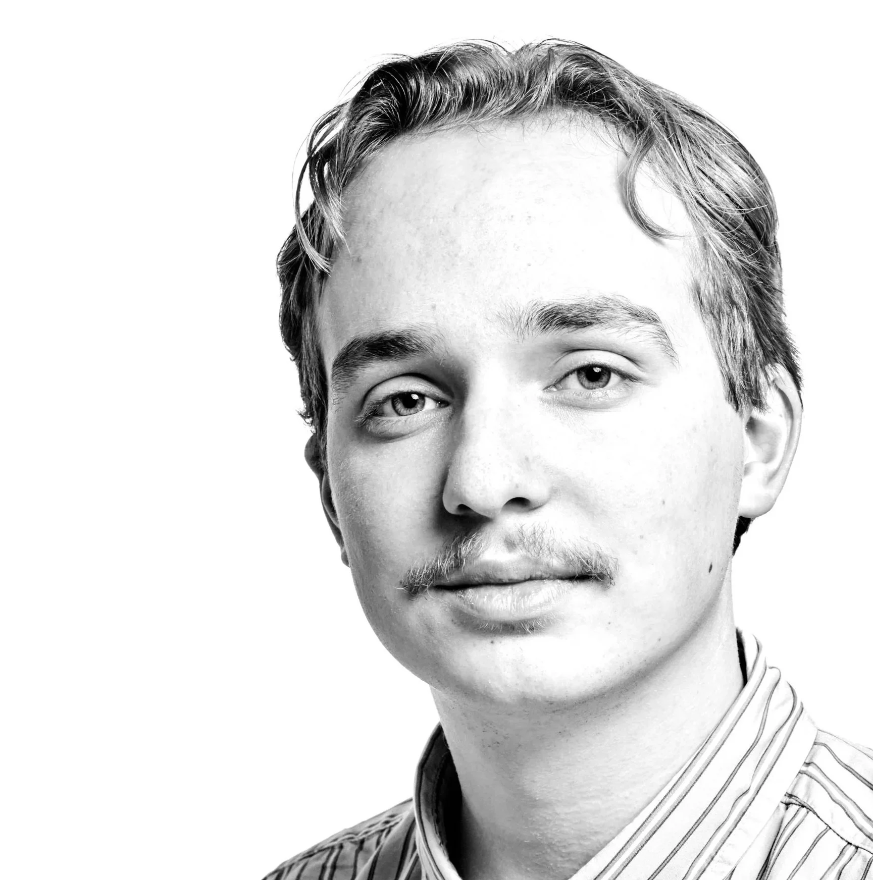 Black and white portrait of a young man with light skin, short wavy hair, wearing a vertically striped collared shirt, against a plain white background.