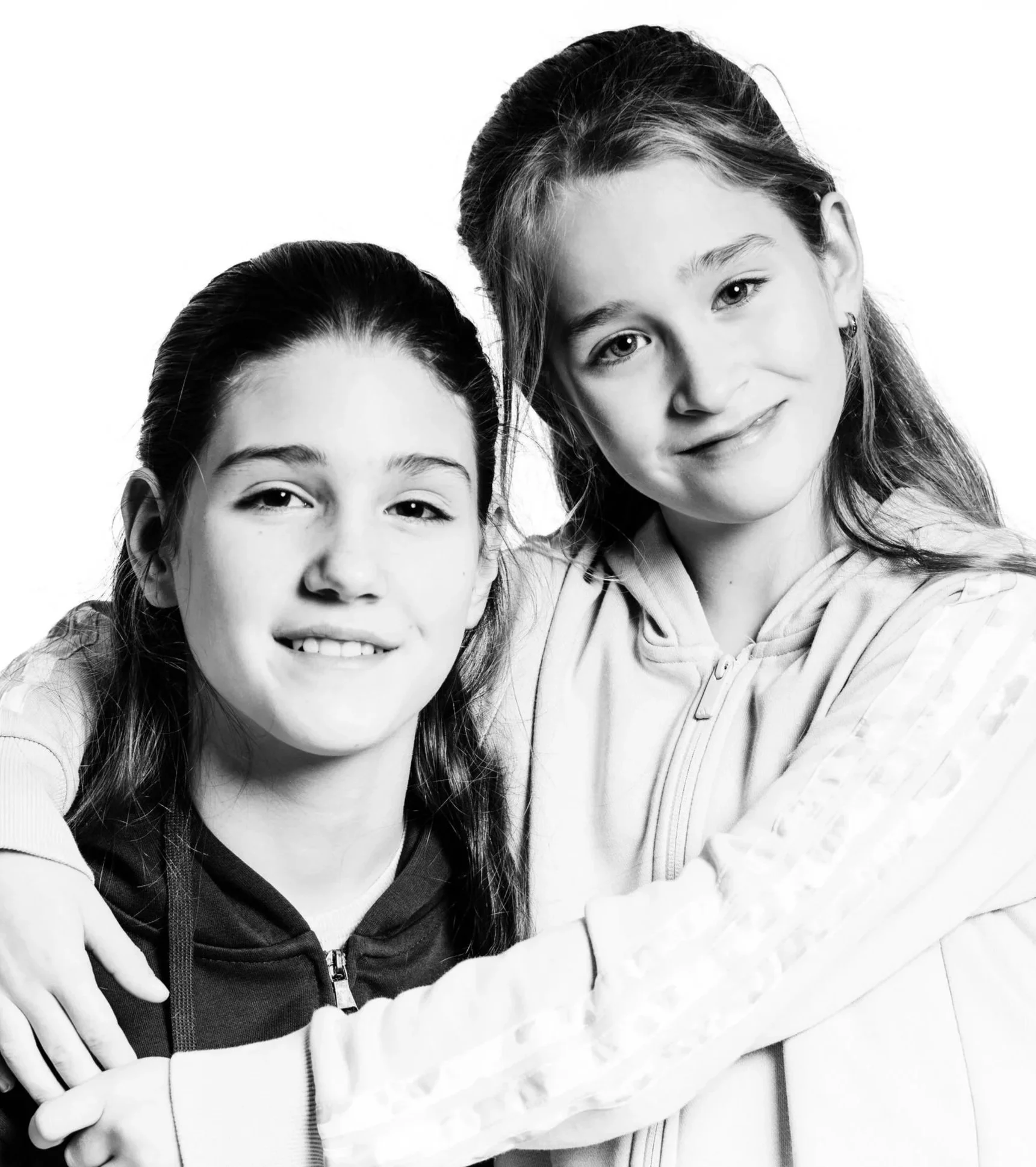 Twee jonge meisjes glimlachen, een met haar armen om de ander heen, zwart-wit foto.