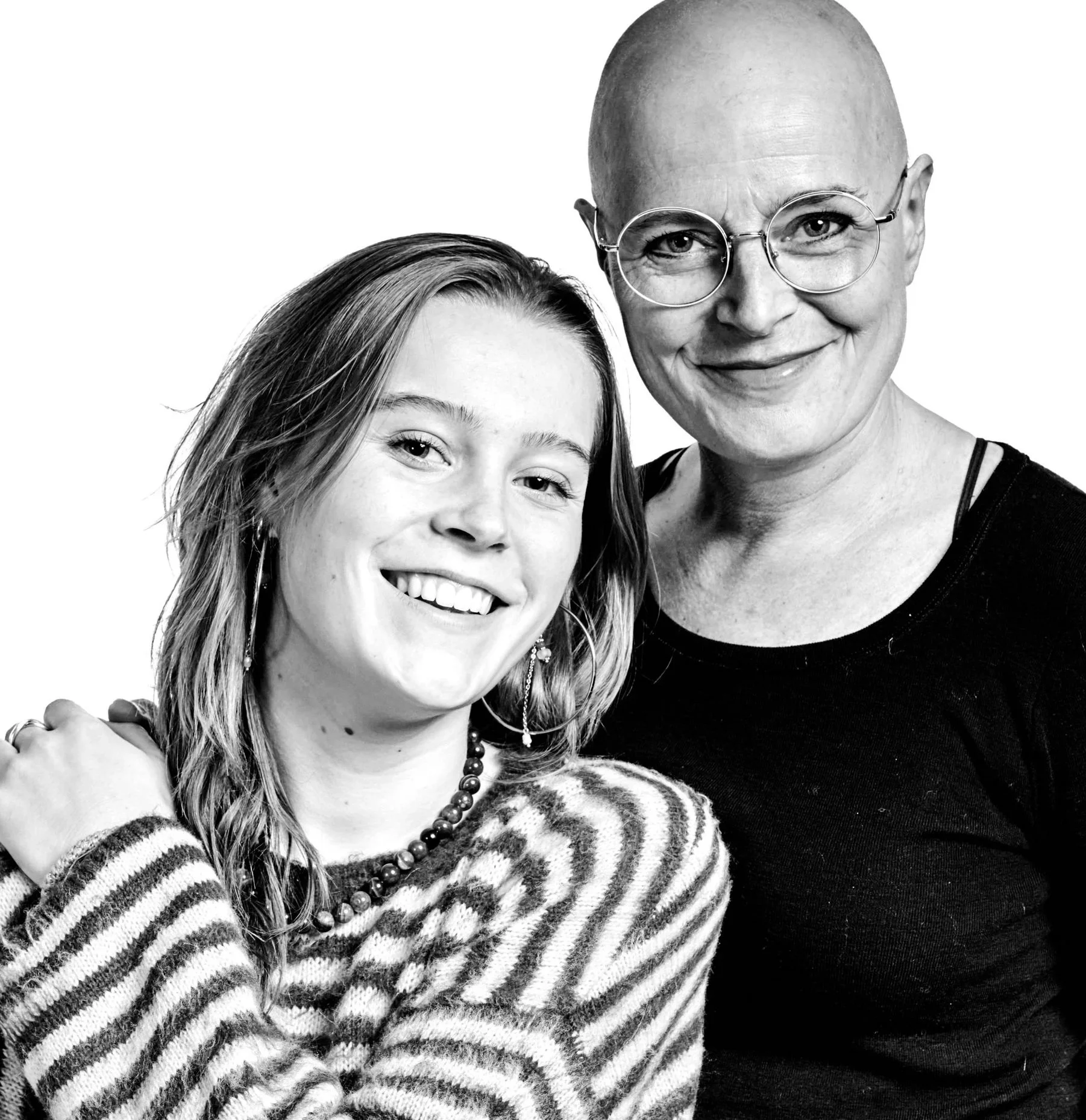 A smiling woman with a shaved head wearing glasses, and a young girl with long hair, both smiling at the camera.
