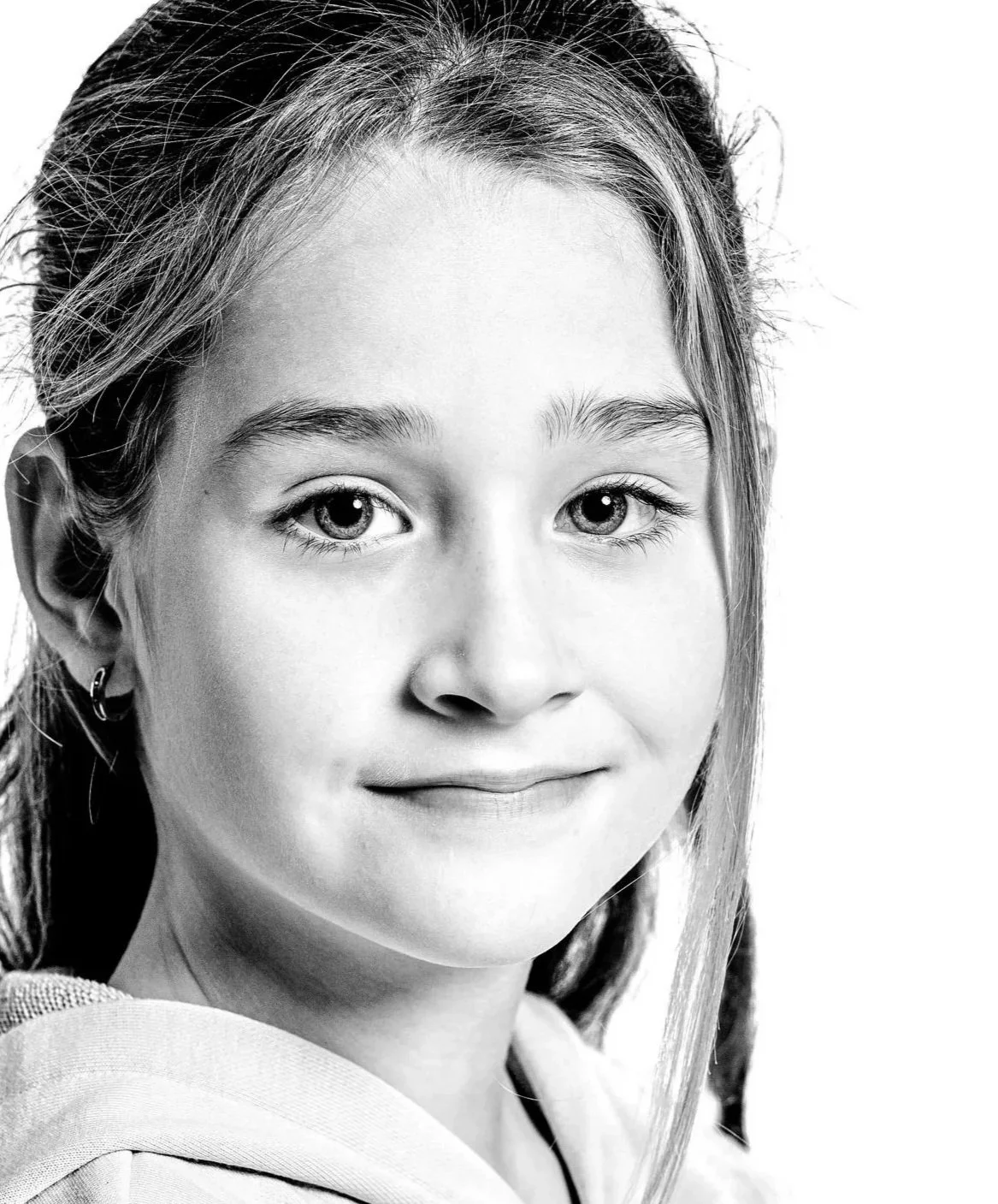 Close-up black-and-white portrait of a young girl with curly hair, wearing a jacket, looking directly at the camera against a plain background.