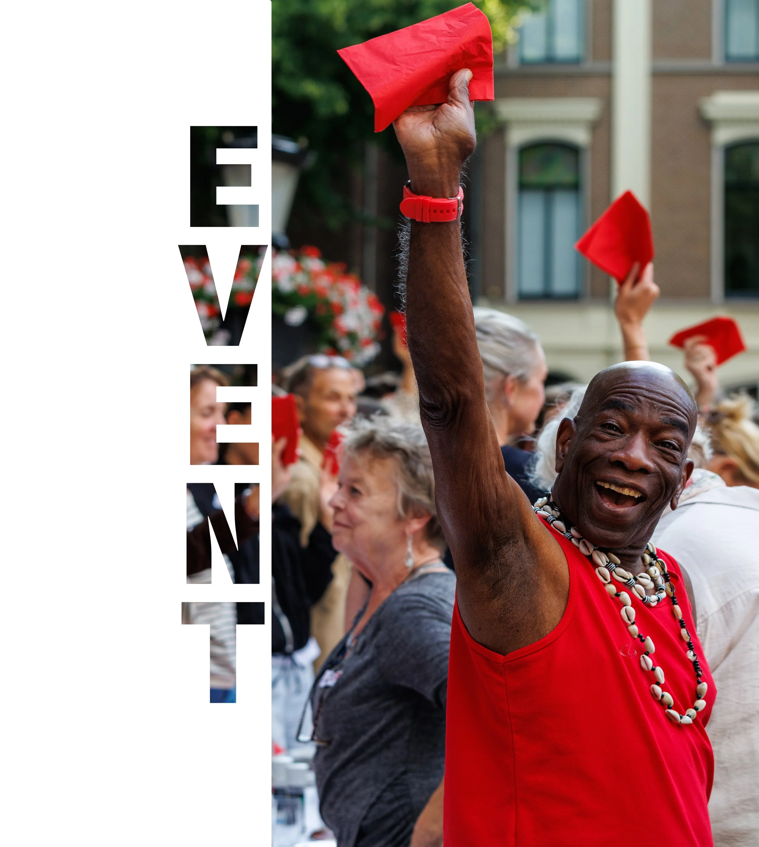 Diverse mensen die deelnemen aan een protest of demonstratie, met een vrouwelijke persoon in rood kunstig gekleed met een ketting en armband, die haar vuist omhoog steekt met een rood doek in de hand, op de achtergrond een stoeprand en een gebouw.