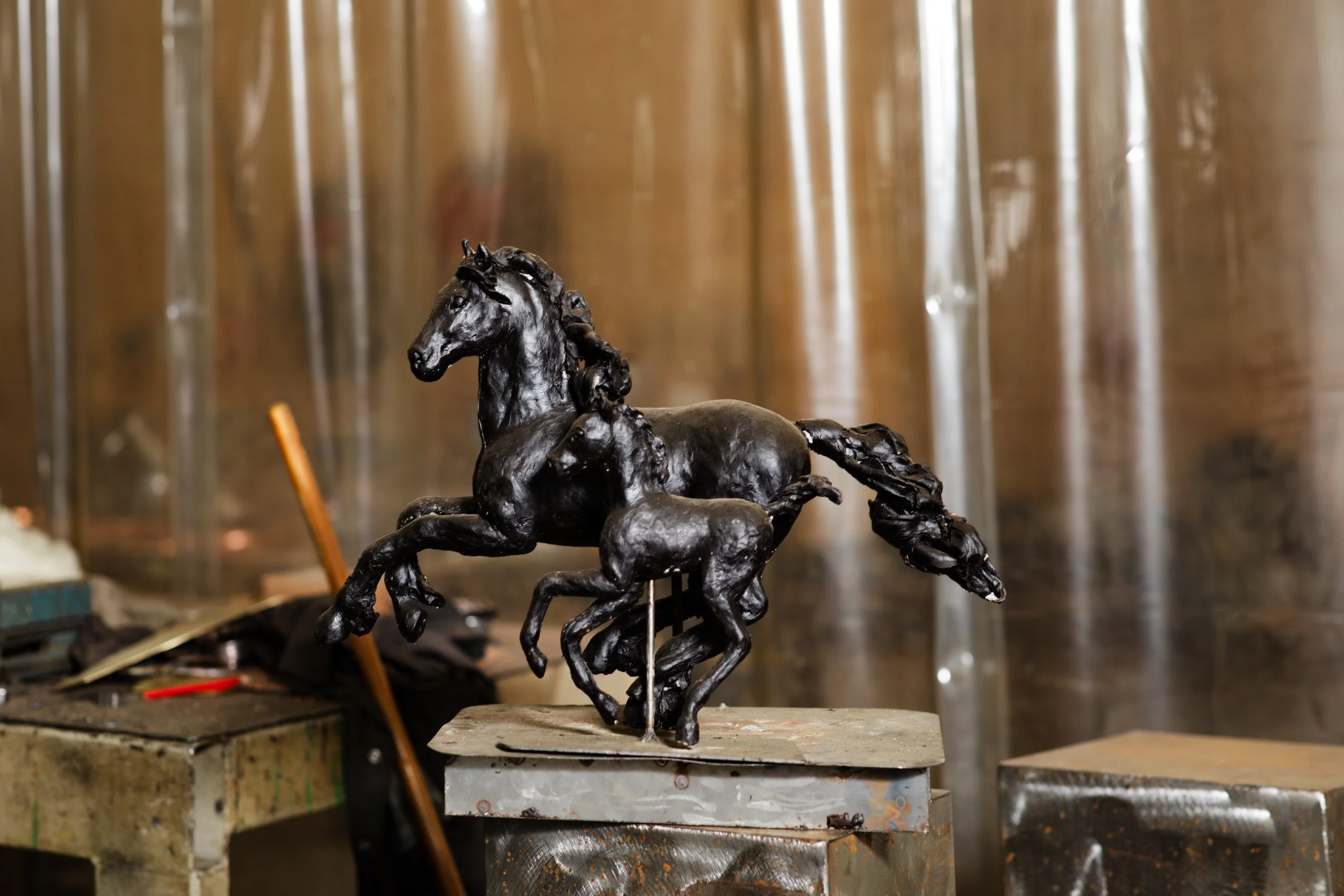 Een bronzen beeld van een springend paard in een artistieke stijl, geplaatst op een houten ondergrond in een werkplaats of atelier.