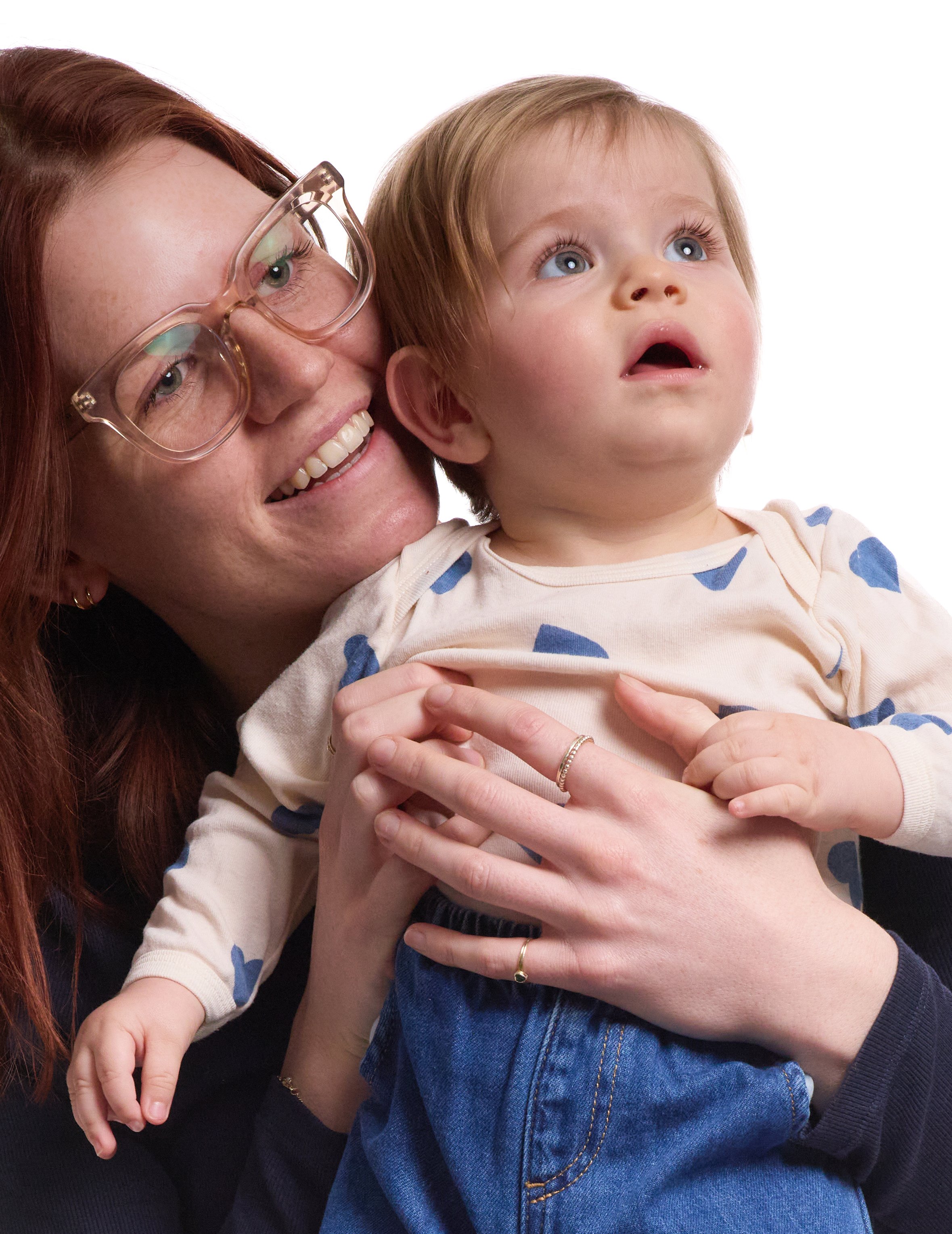 Een vrouw met rood haar en bril houdt een kind met blauwe ogen en lichtbruin haar vast.