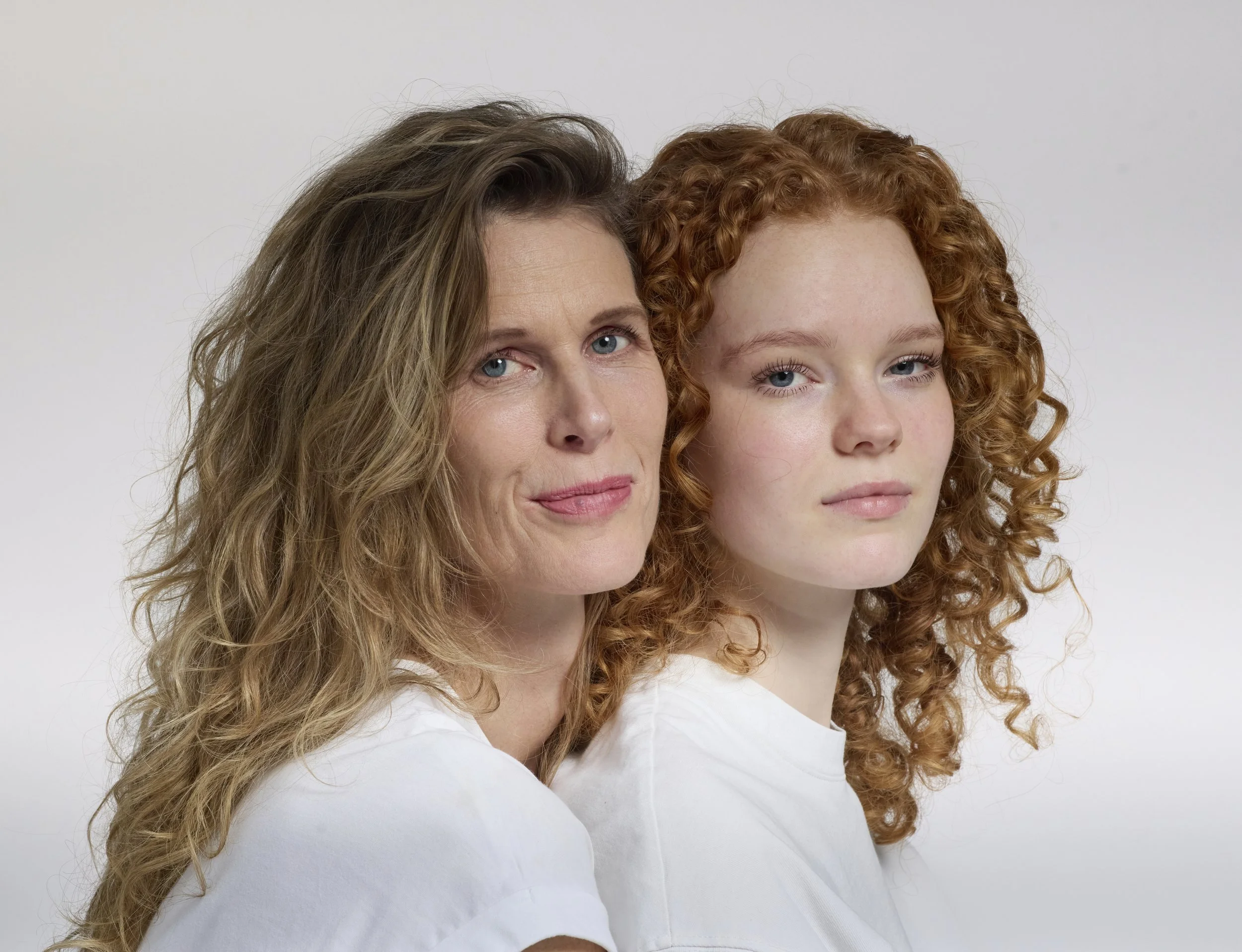 Two women with curly hair, one with brown and blonde hair, the other with red hair, posing against a plain background.