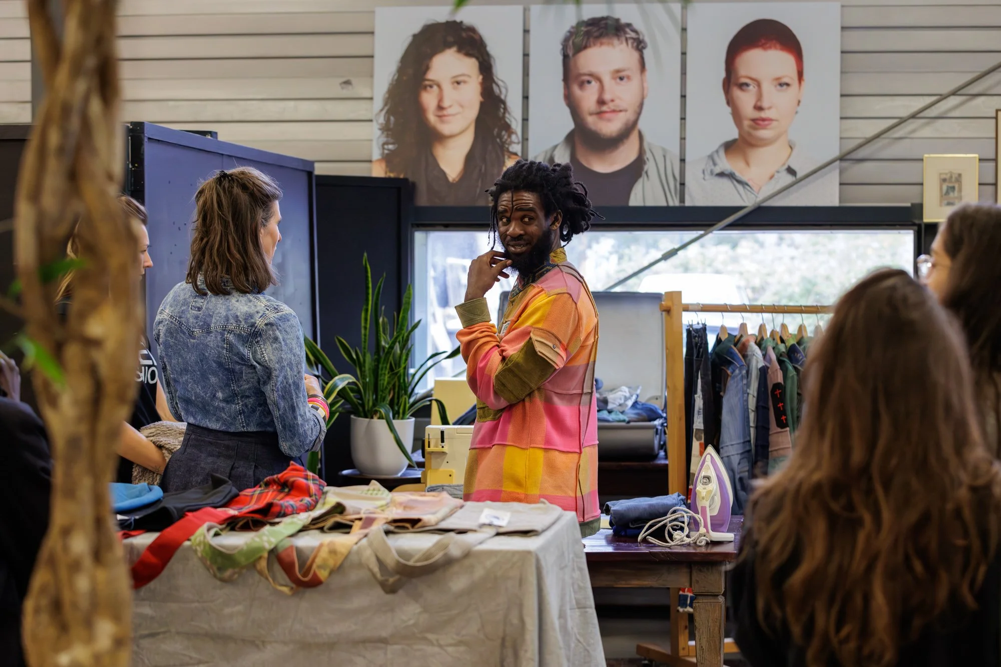 People browsing clothing and fabric at a flea market or thrift store with large portraits on the wall behind them.