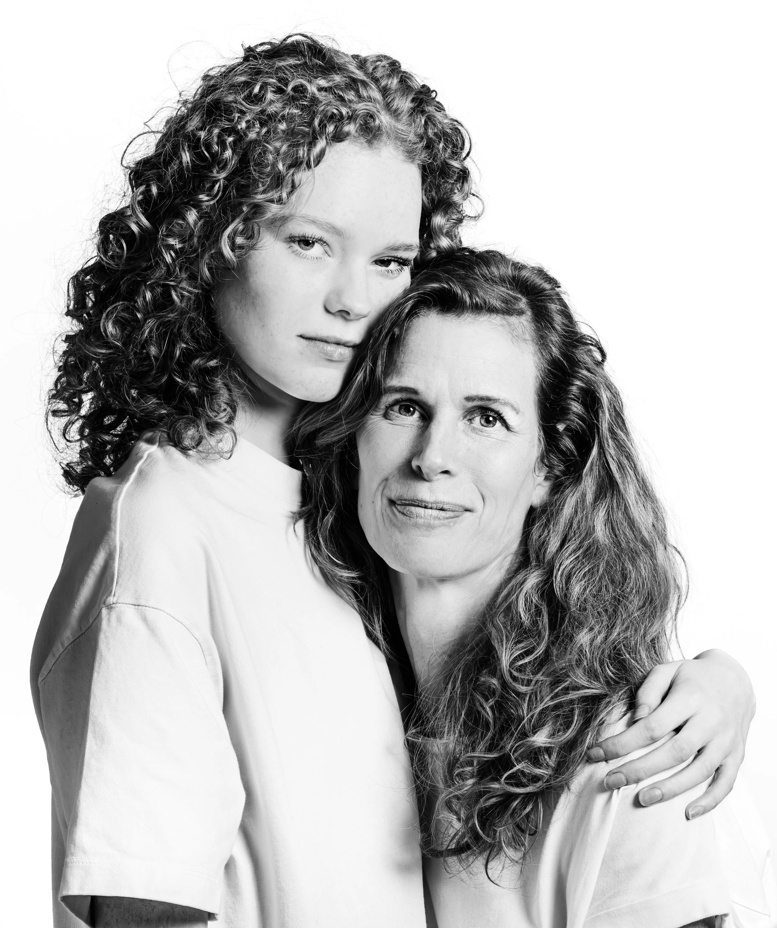 Black and white photo of a young girl with curly hair embracing a woman, both with serene expressions.