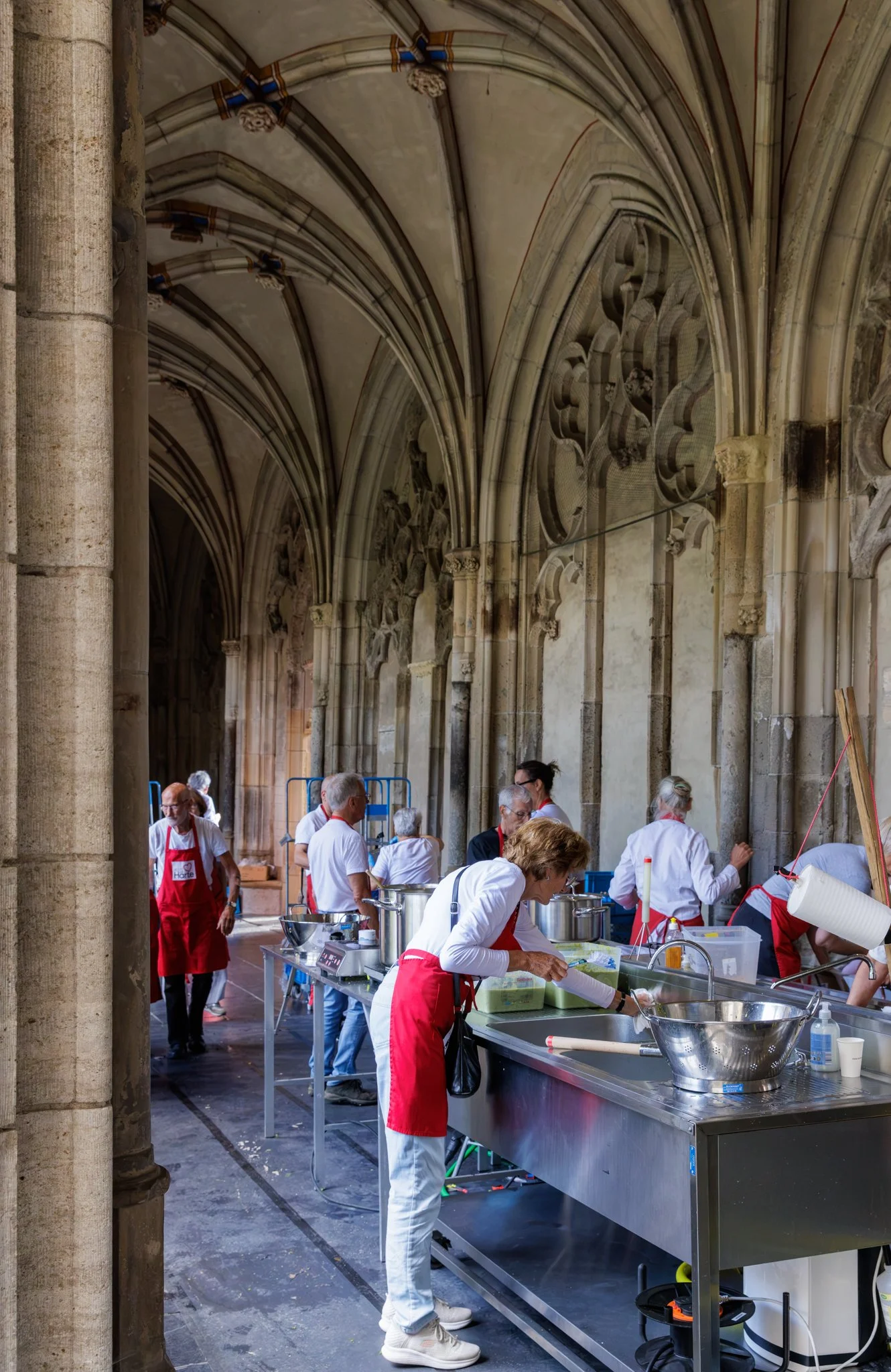 Mensen in een oude kerk doen vrijwilligerswerk, koken en bereiden eten, met veel keukengerei en kolven, onder hoge gewelfde plafonds.