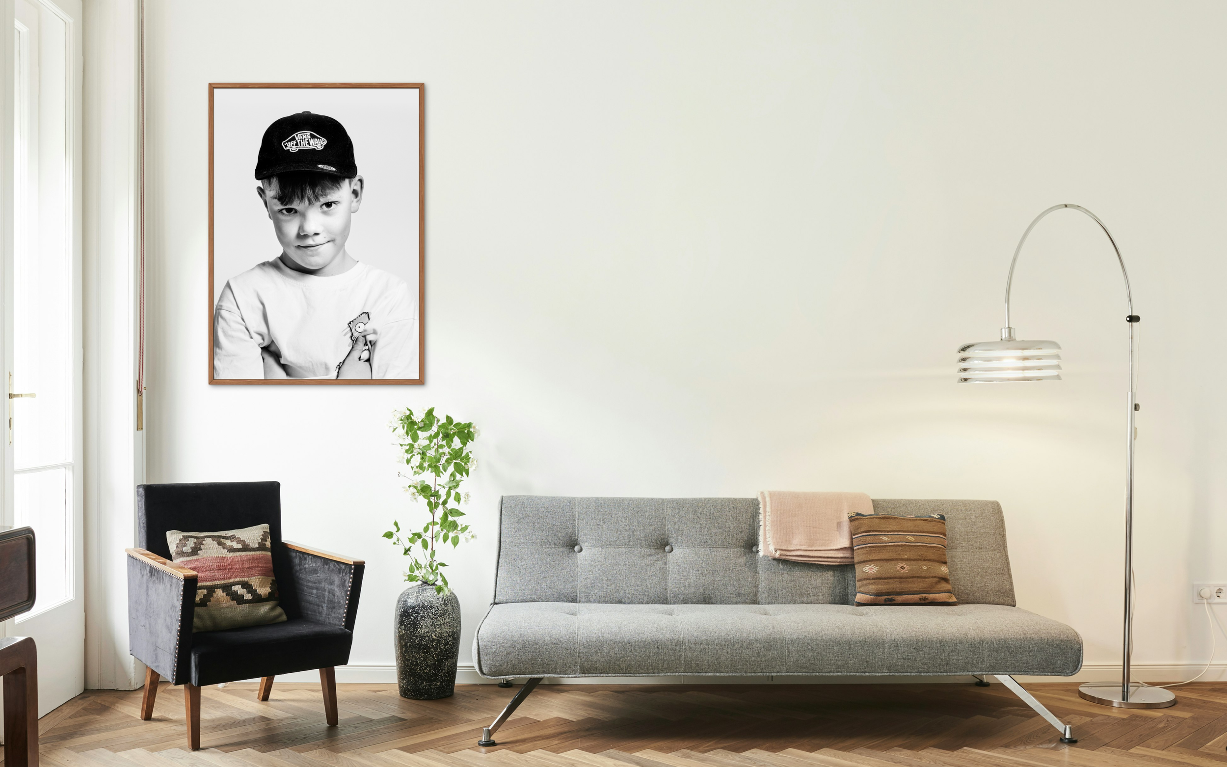Living room with a black armchair, grey sofa, potted plant, a framed black and white photograph of a boy on the wall, and a modern floor lamp.