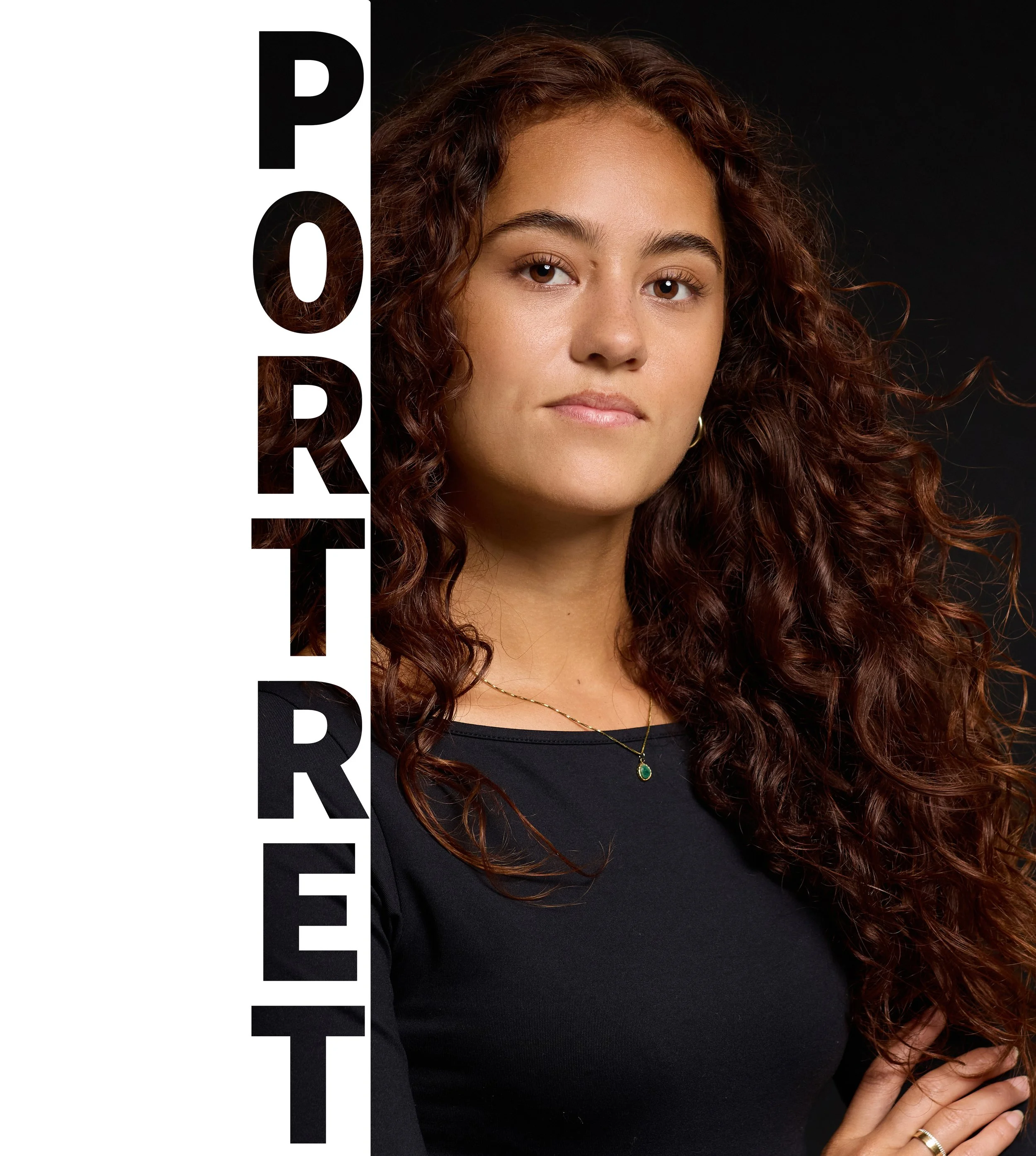 Portret van een jonge vrouw met krullend bruin haar, zittend tegen een zwarte achtergrond, met een ringen- en kettingaccessoire.