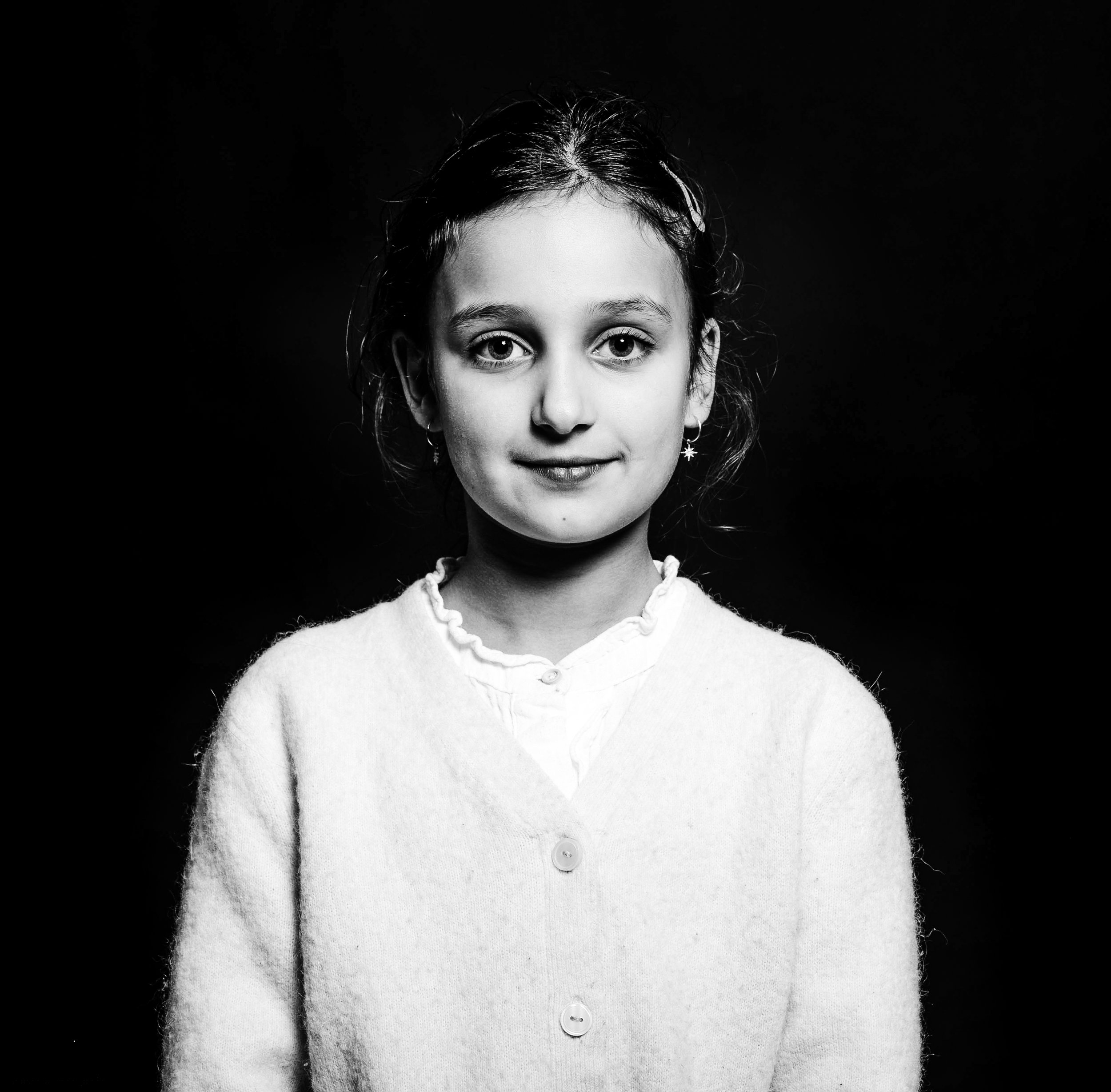 Black and white portrait of a young girl with a slight smile, wearing a buttoned cardigan and star-shaped earrings.