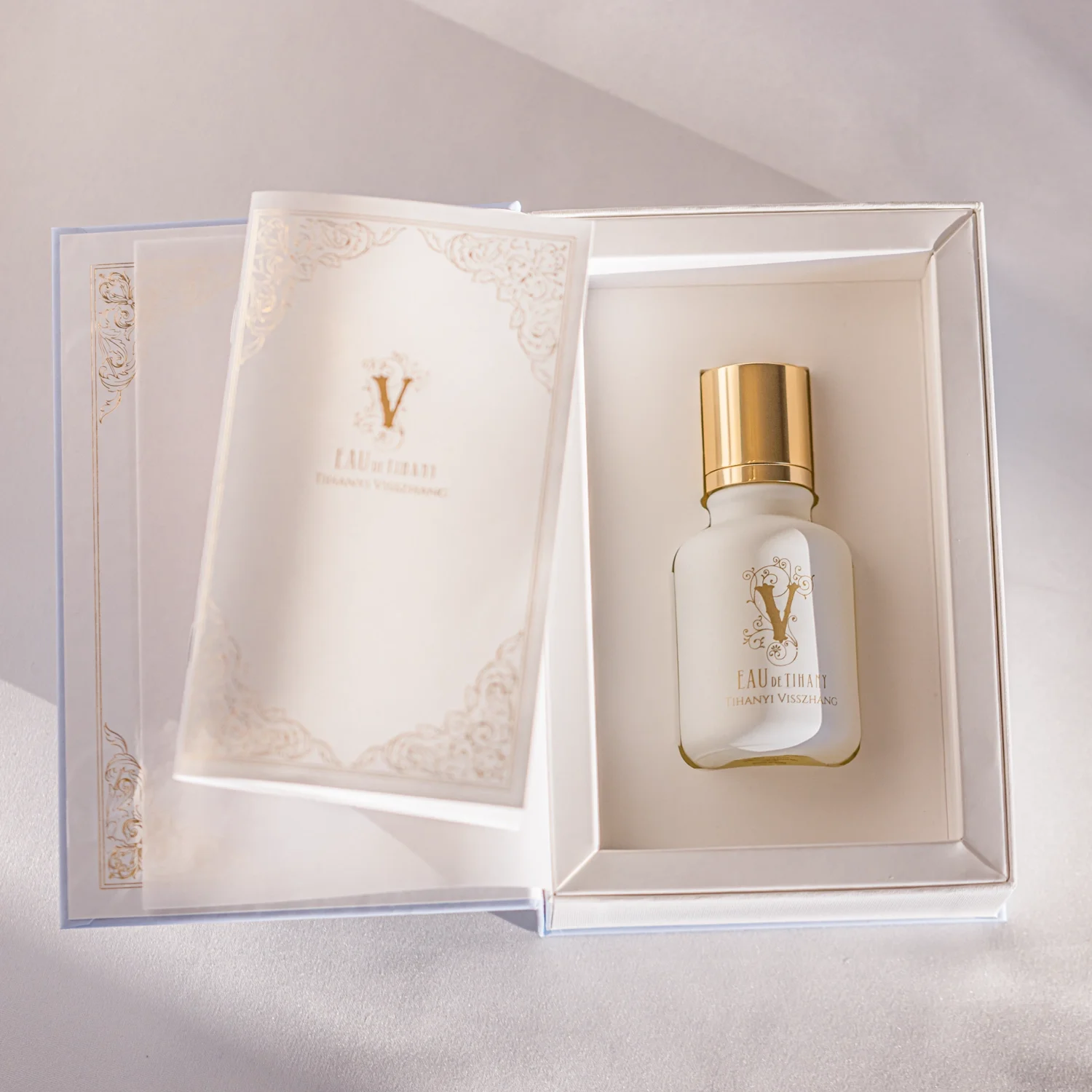 A luxurious perfume bottle labeled 'Eau de Tihanyi' with a gold cap, nestled in a white box with ornate cards, bathed in soft natural light.