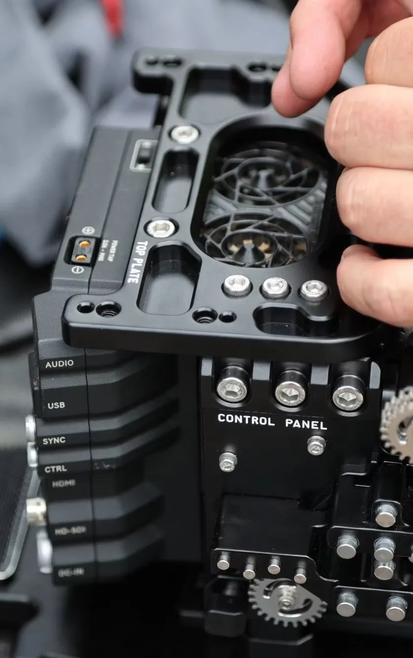 Close-up of a person assembling a large professional camera or cinema camera, focusing on the top plate and control panel.