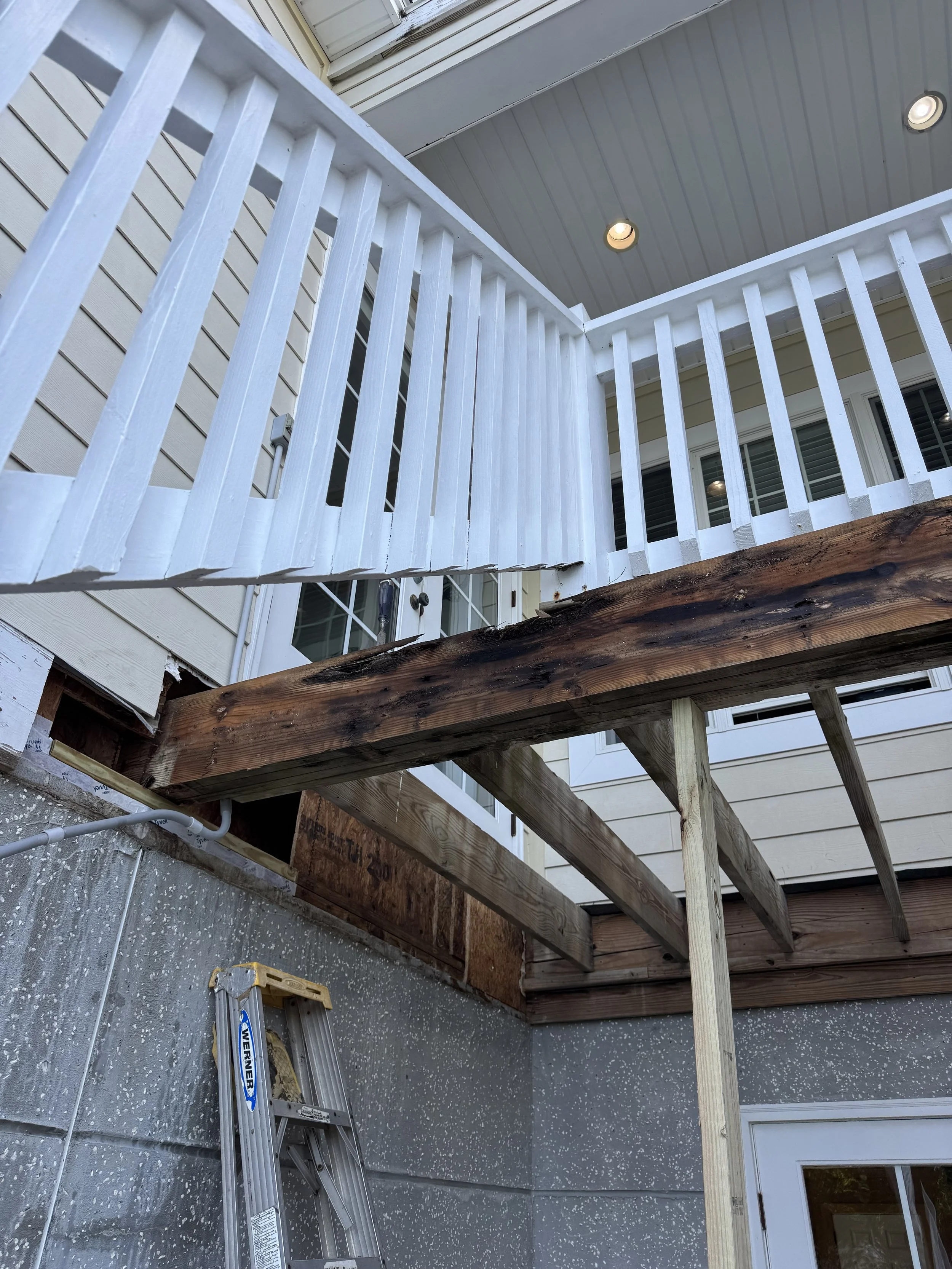 A person wearing a mask and gloves is working on a home renovation project, removing or repairing the wooden floor in a partially demolished room with exposed walls and construction tools around.