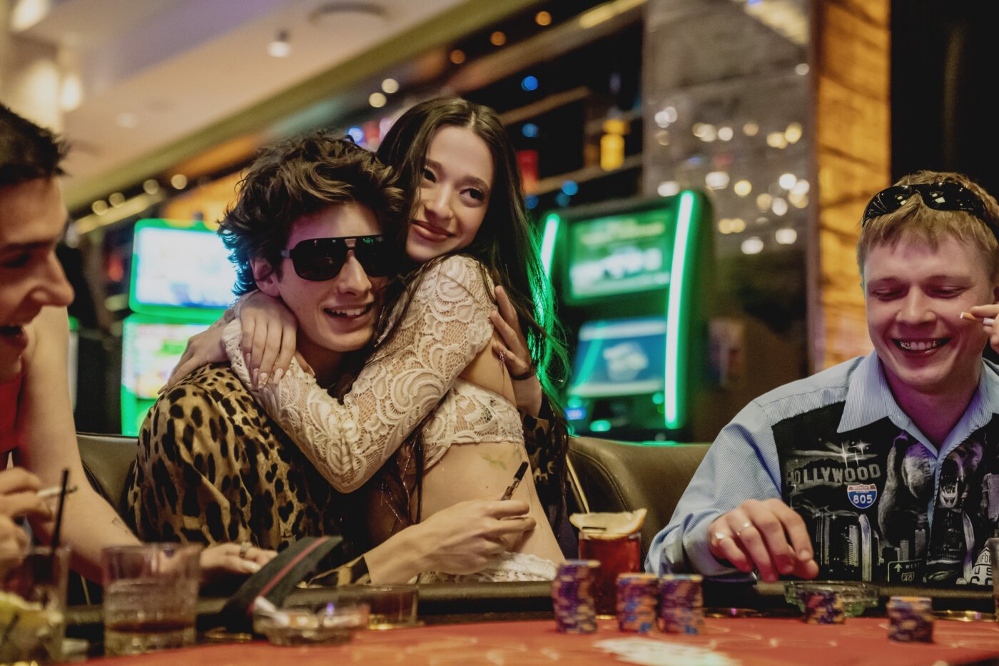 Ani and Ivan embrace at a casino table in Anora, surrounded by neon lights and gamblers, capturing the film’s chaotic early energy.