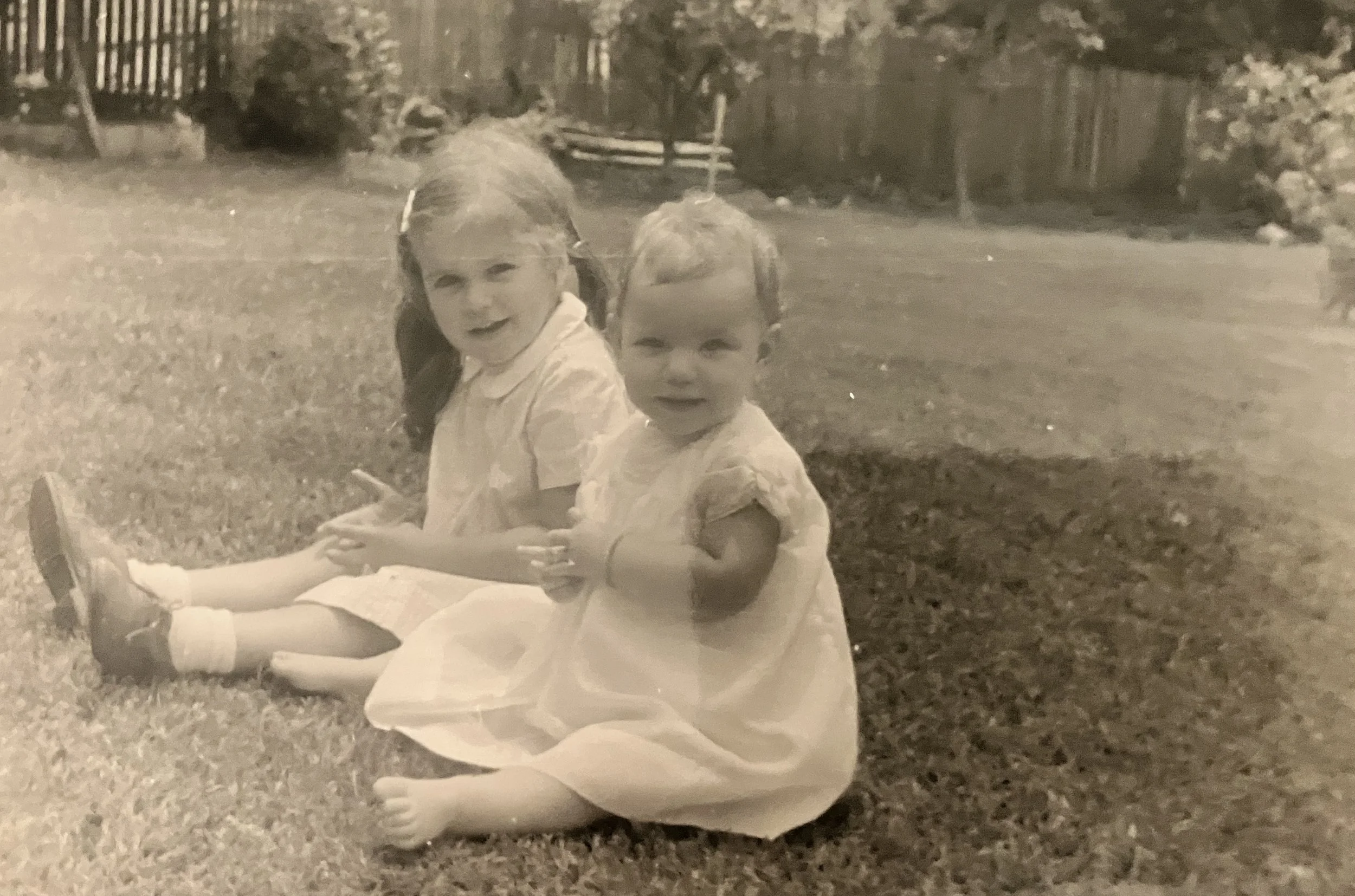 A black and white photo of two little girl sitting on the grass circa 1970