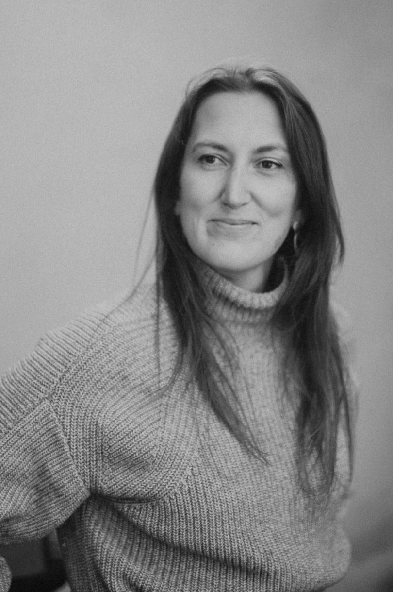 Black and white photo of a woman wearing a turtleneck sweater, smiling gently, with long dark hair.