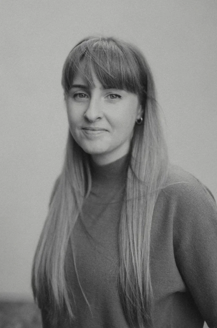 Black and white portrait of a woman with long straight hair, wearing a turtleneck sweater and small hoop earrings, smiling softly against a plain background.