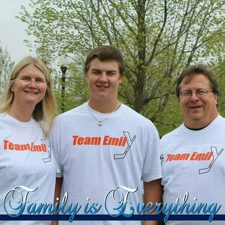 Family photo outdoors with three people wearing matching 'Team Emil' t-shirts, standing in front of trees, with the text 'Family is Everything' at the bottom.
