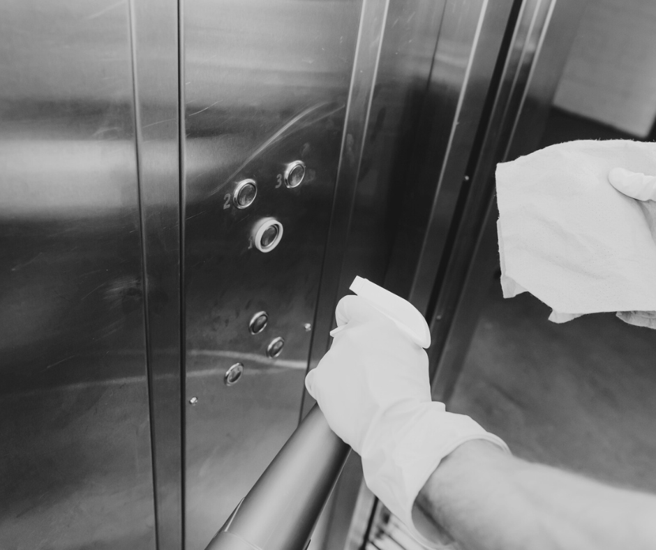 Worker cleaning elevator buttons with disinfectant spray, representing healthcare cleaning services and sanitation standards applied in multi-family or high-traffic buildings.