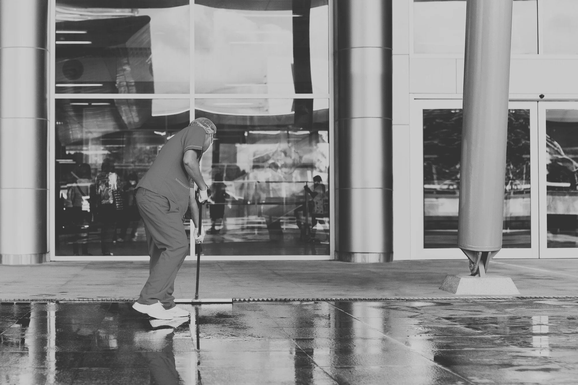 Professional commercial cleaning services worker mopping exterior entrance of office building during seasonal maintenance audit