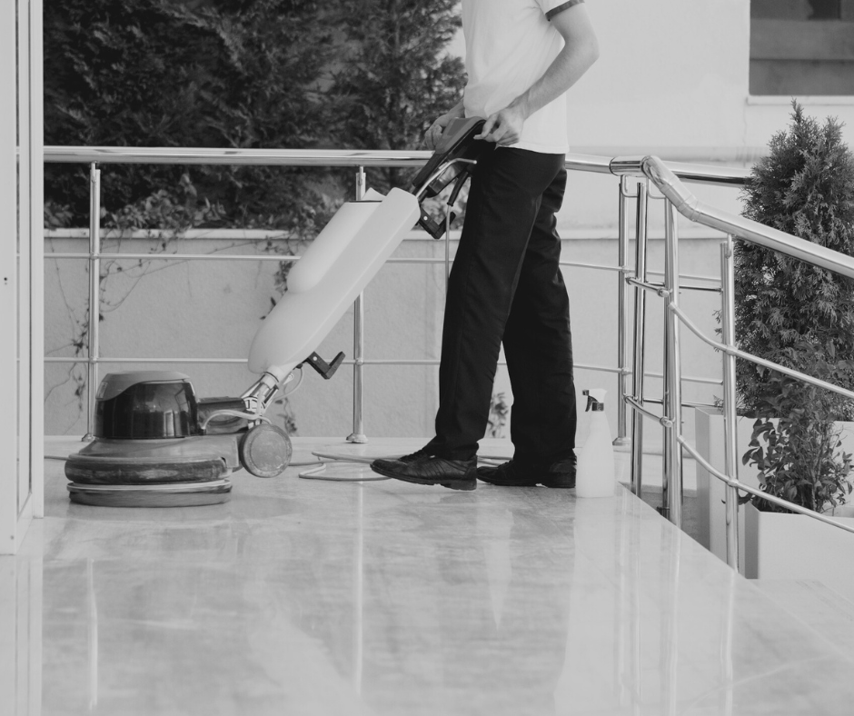 Professional cleaner using a floor scrubber machine on a building entrance, representing commercial building cleaning services that maintain safety and business continuity.