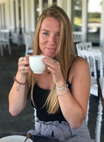 A woman with long blonde hair holding a white coffee cup at a restaurant or cafe.