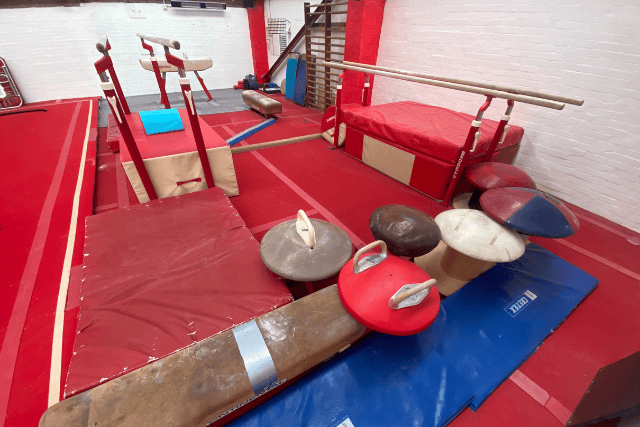 Gymnastics training area with mats, vaulting equipment, and balance beams in red and blue colors.