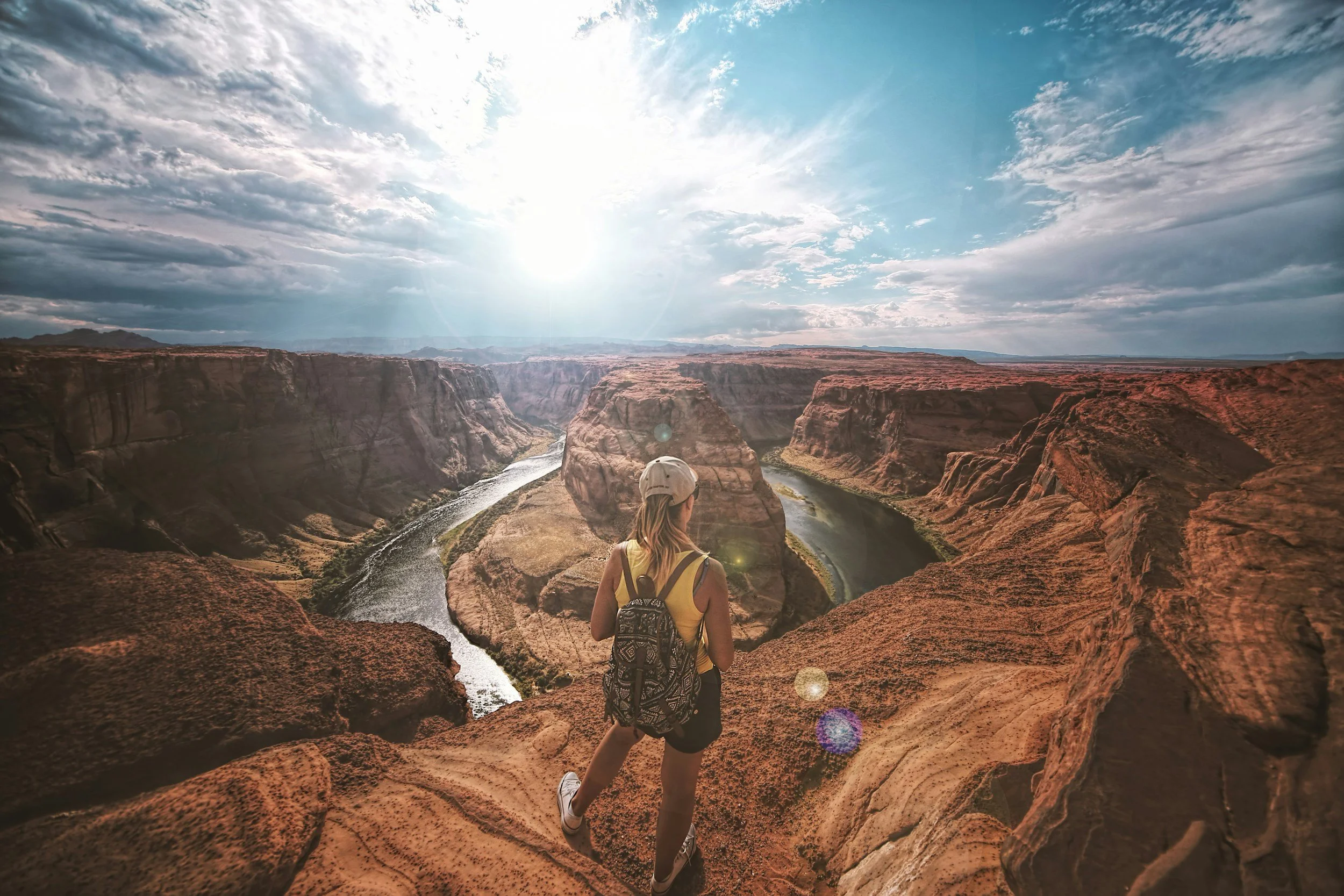 Woman standing at the top of Horseshoe Bend overlooking the landscape.
