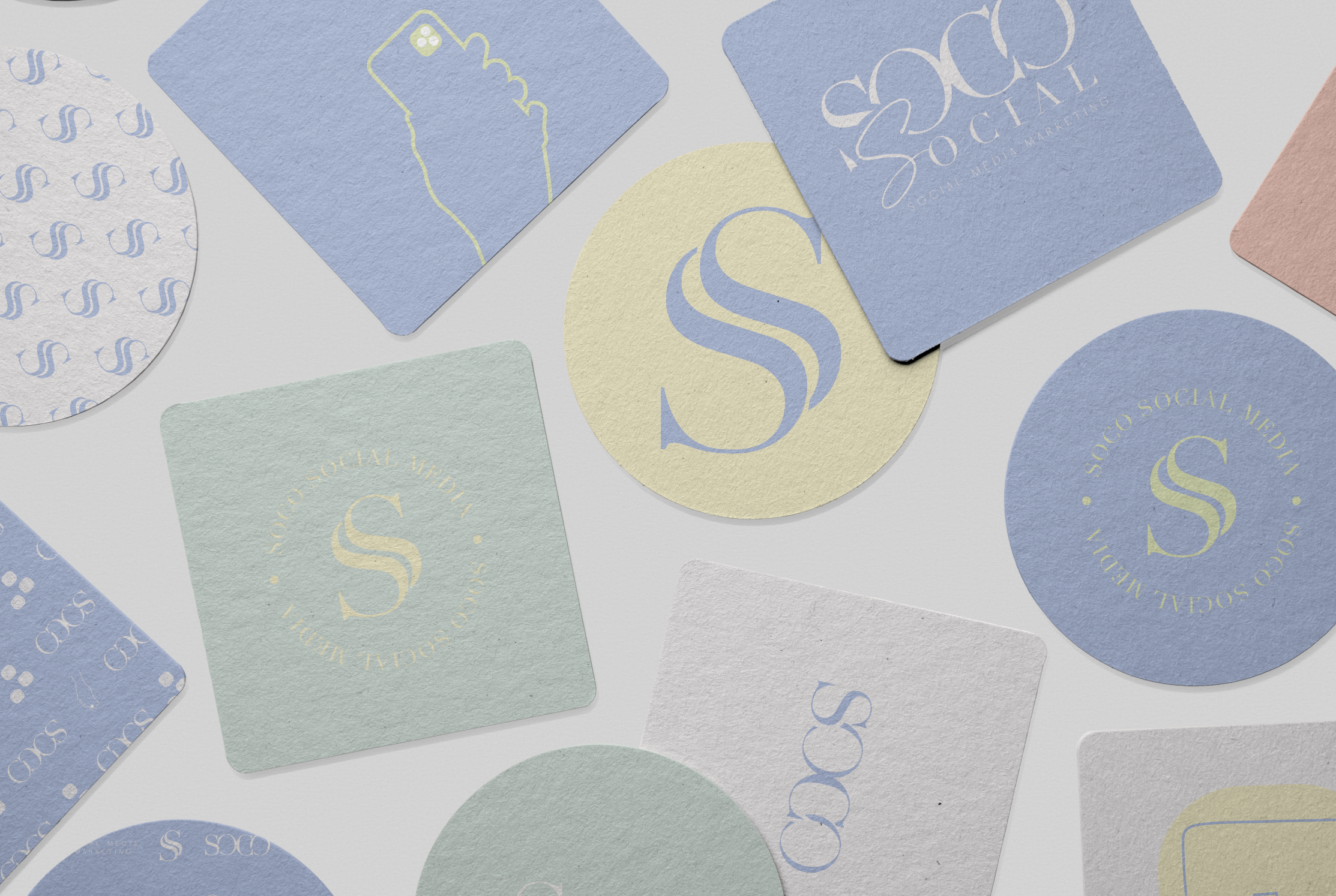 Various pastel-colored printed marketing materials, including business cards, stickers, and round tags, featuring the logo and branding for SOCO Social Media.