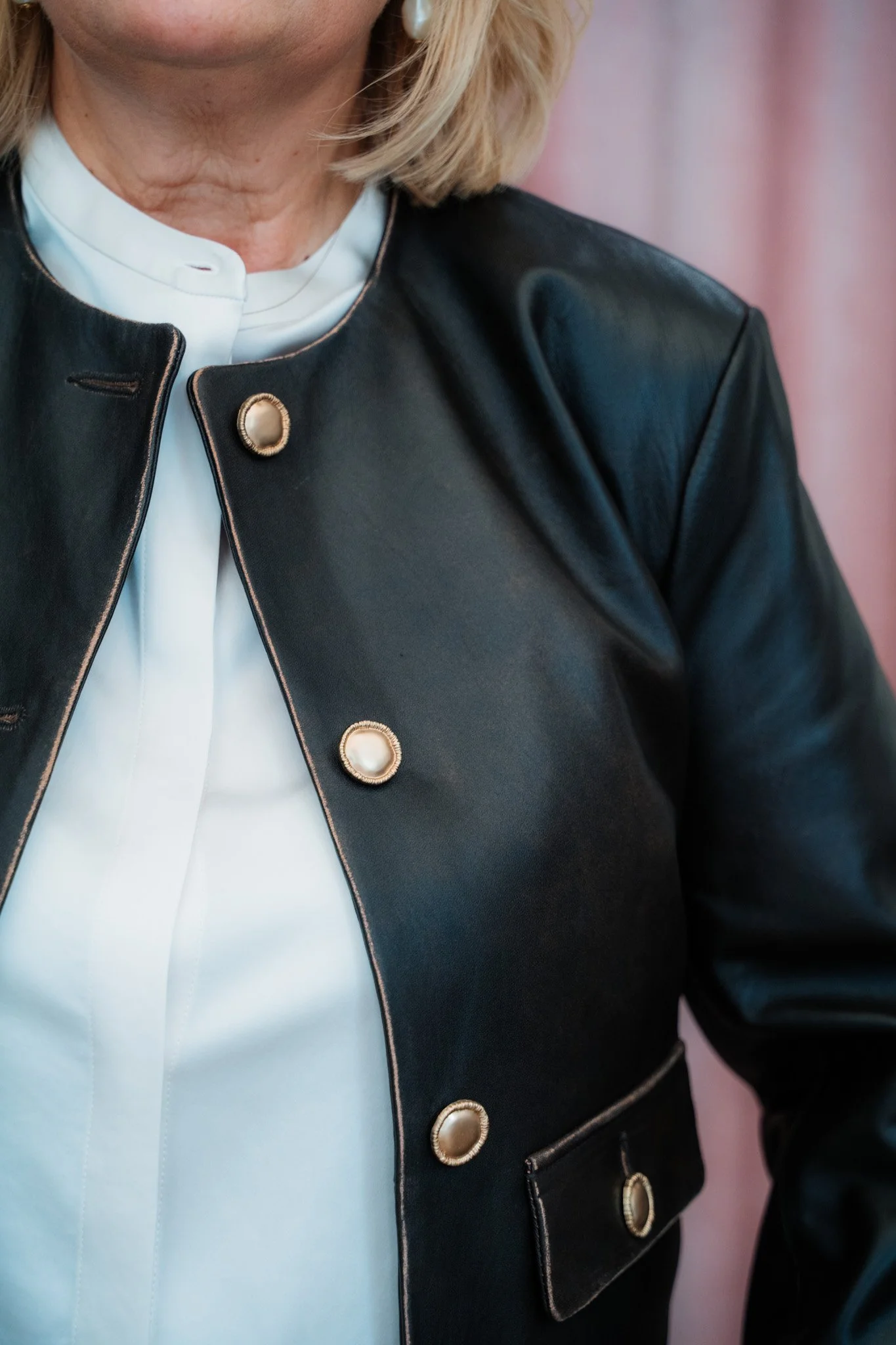 Eine nahaufnahme einer Person, die eine schwarze Lederjacke mit goldenen Knöpfen und eine weiße Bluse trägt.