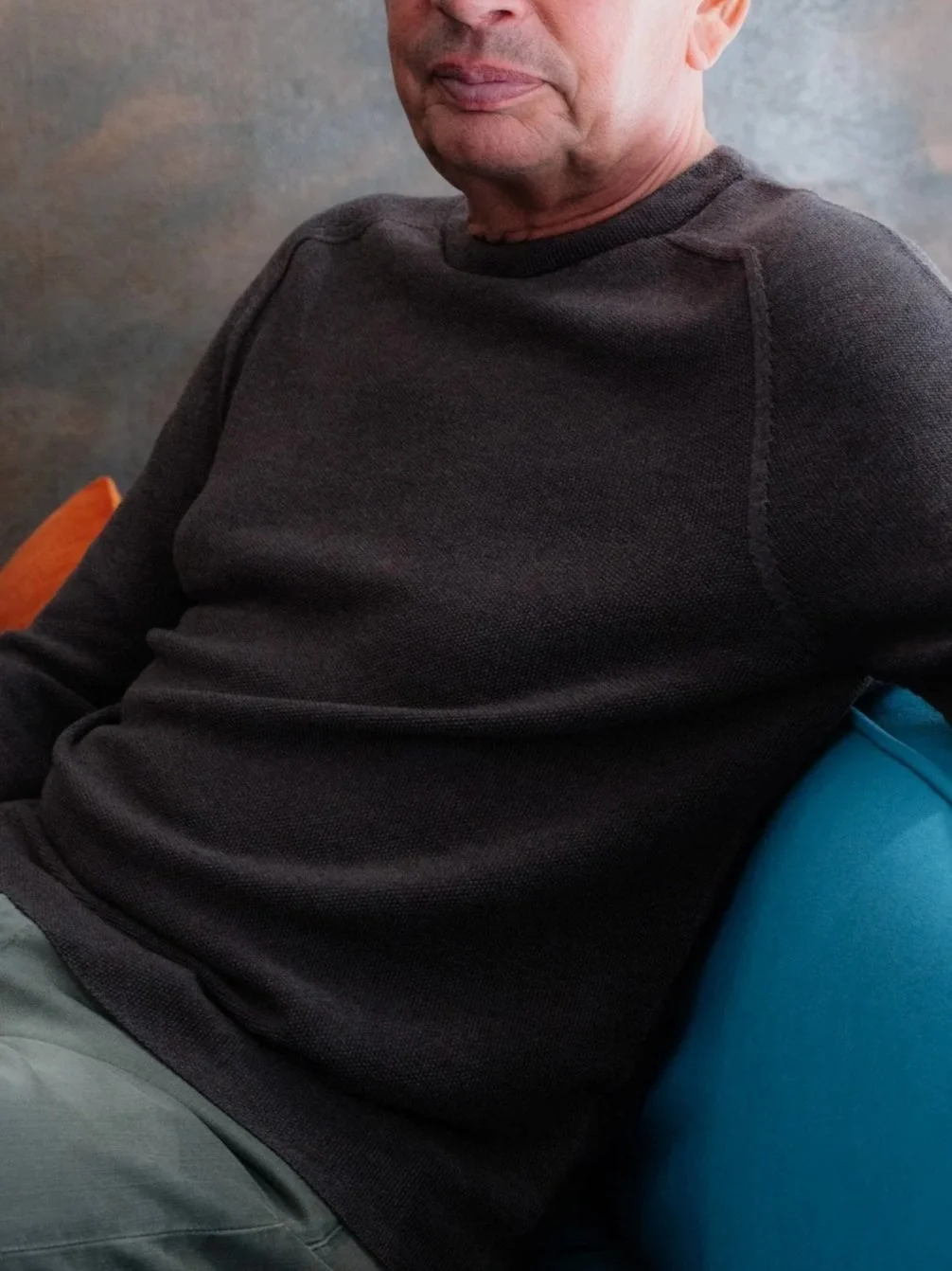 Nahaufnahme eines Mannes, der einen schwarzen Pullover trägt, sitzend auf einem bunten Stuhl.