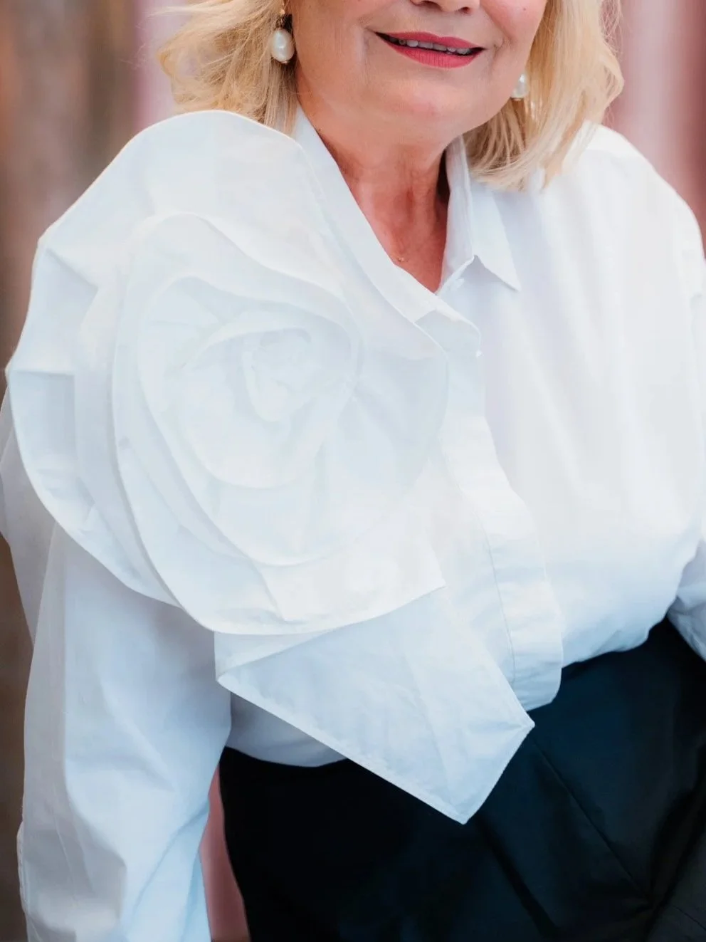 Nahaufnahme einer Frau mit blonden Haaren, die ein weißes Hemd mit großen, gepufften Ärmeln trägt und lächelt.