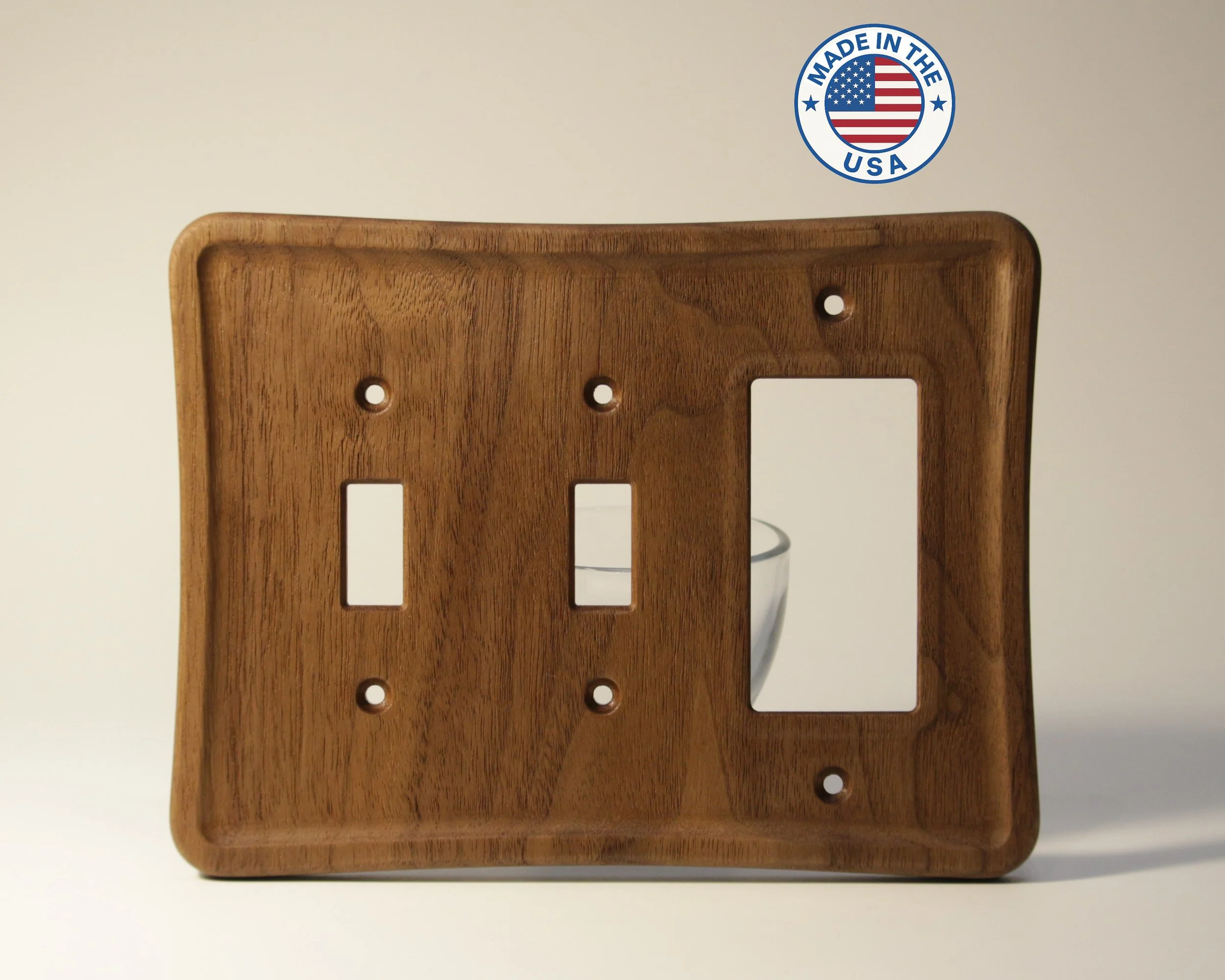 A wooden faceplate or cover, possibly for electrical outlets or switches, mounted on a wall. There are multiple screw holes visible, and the background wall is light-colored.