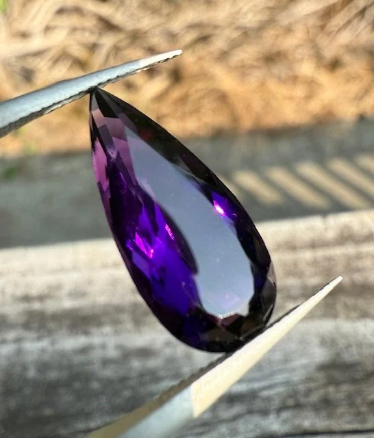 Close-up of a purple gemstone being held with tweezers.