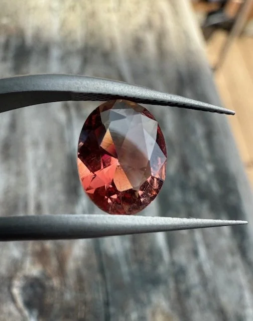Close-up of a faceted oval gemstone held by tweezers with a wooden background.