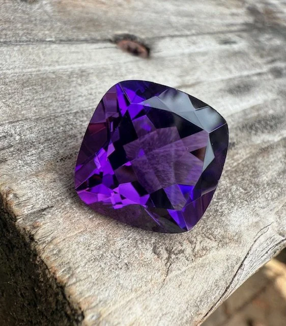 A large, faceted purple gemstone resting on a weathered wooden surface.