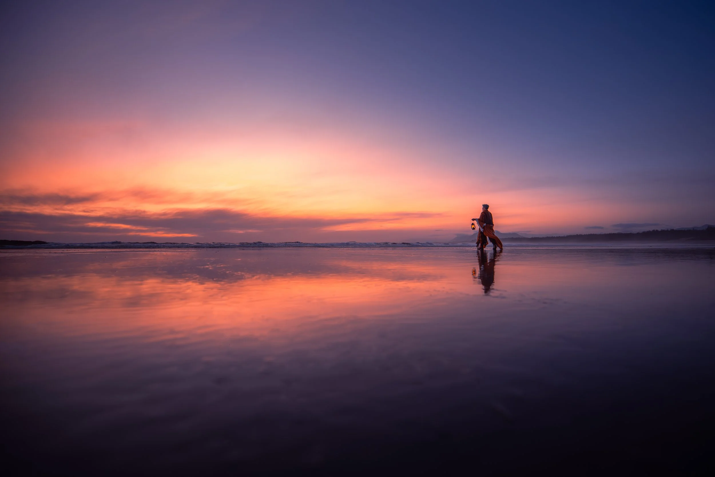 Person walking on a beach during sunset, reflecting in wet sand