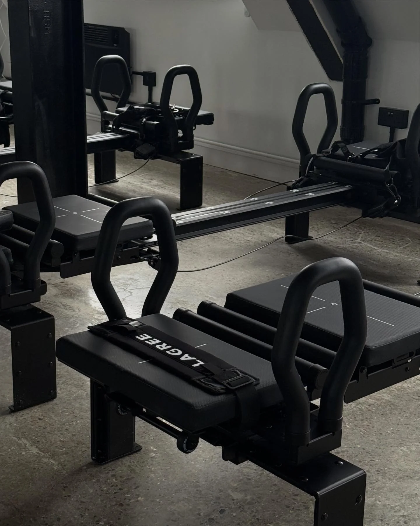 Fitness studio with reformer Pilates machines and black handles on a concrete floor.