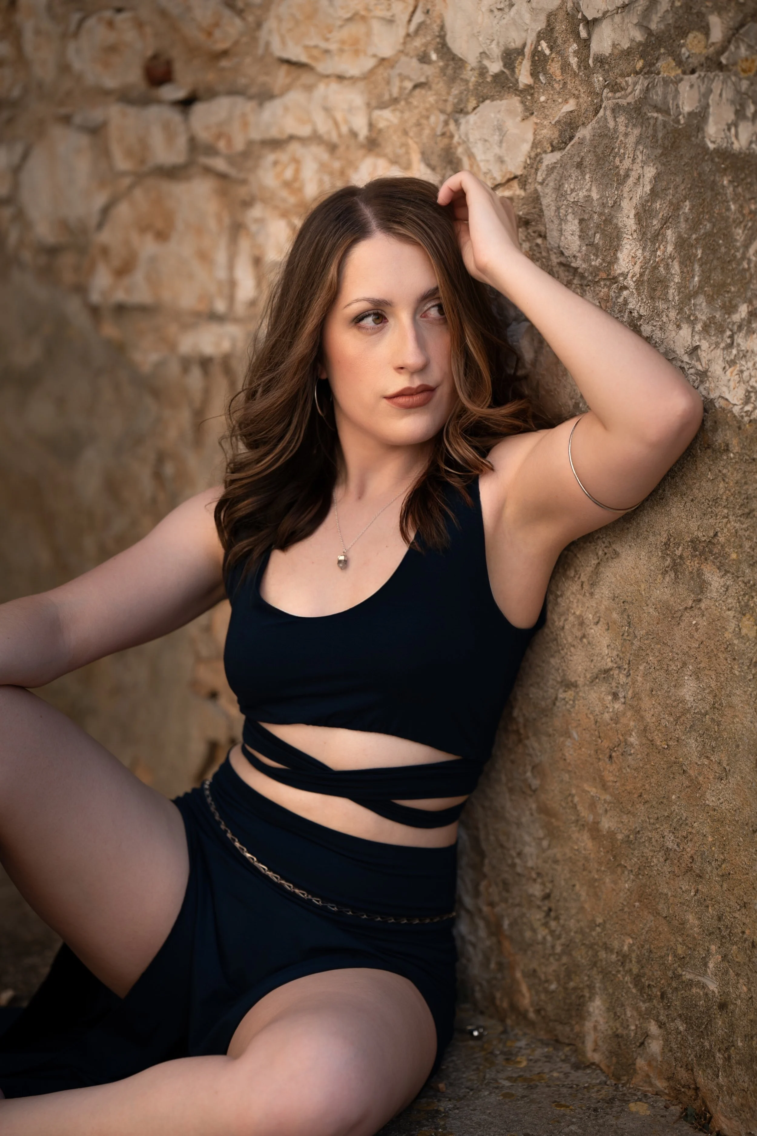 Marley leans against a wall with her arm above her head.