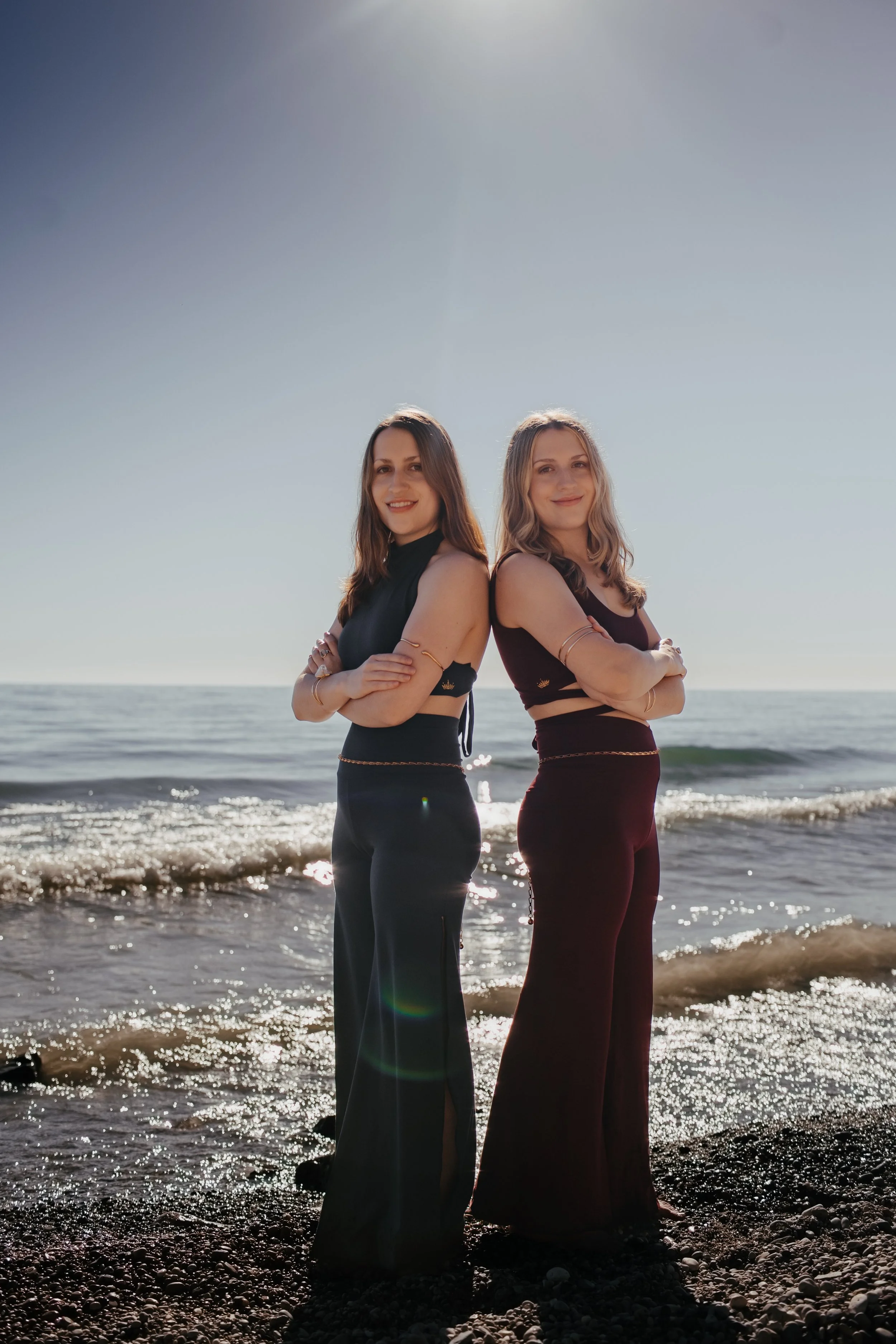 Marley and Lacey stand back to back with their arms crossed on the beach.