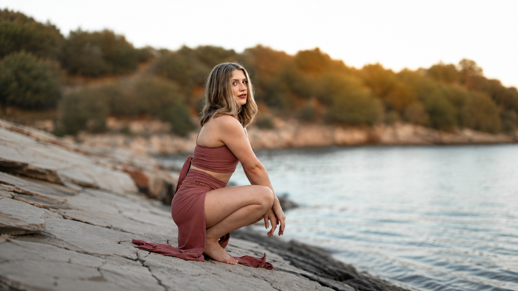 Lacey kneels on a rock in front of the water.