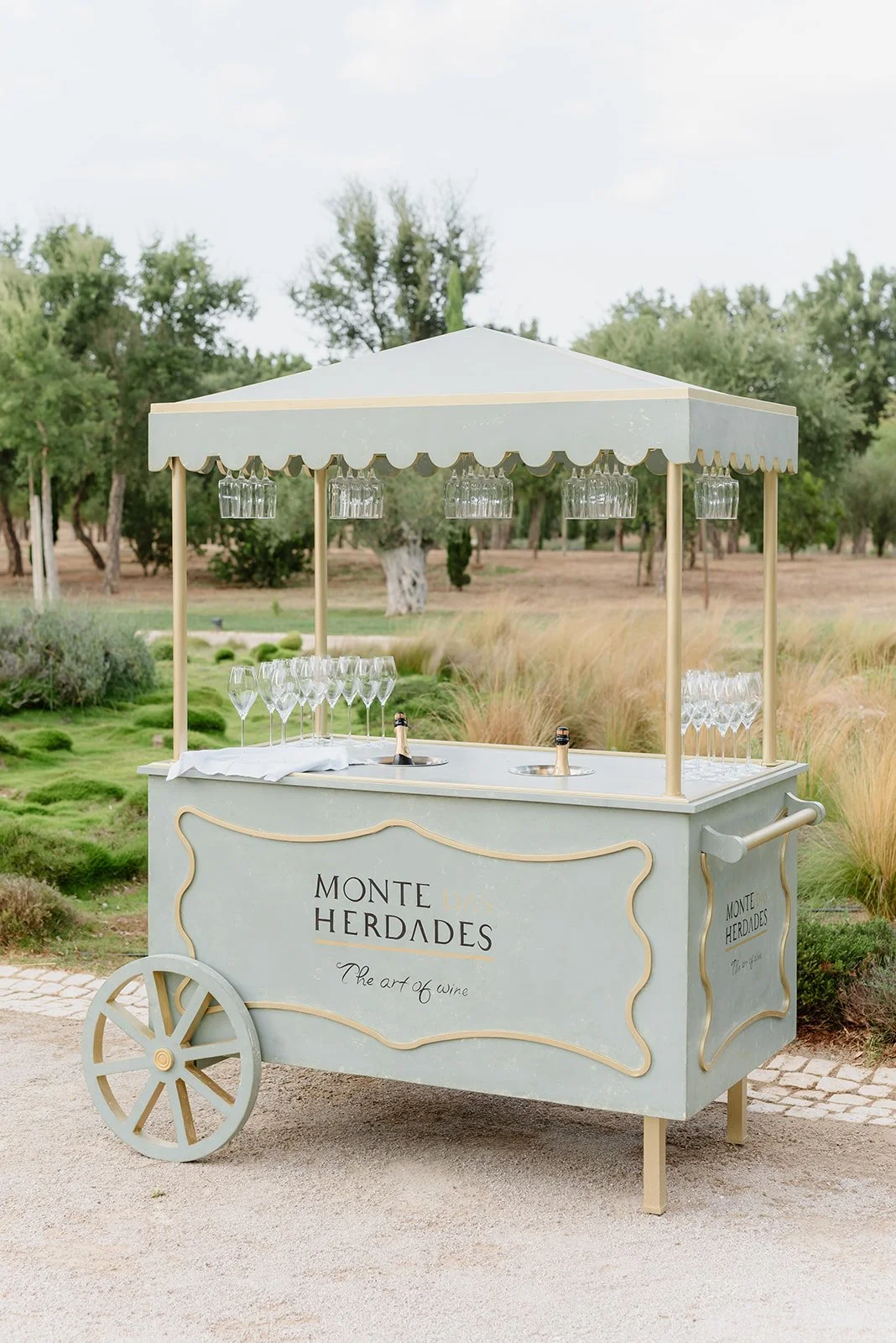 A vintage-style wine and champagne cart with a canopy, glasses, and champagne bottles in a lush outdoor setting.
