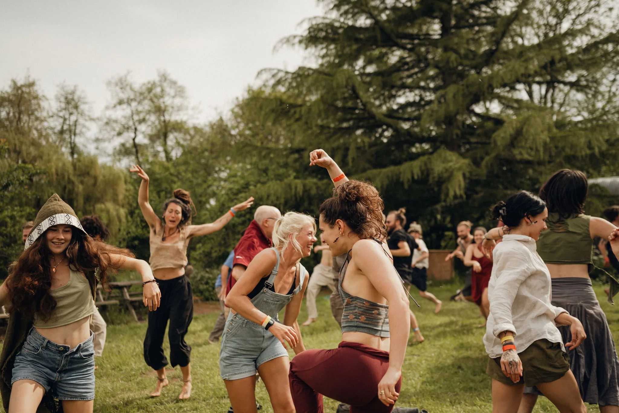 People dancing and laughing outdoors in a grassy area with trees in the background during a festival or outdoor event.